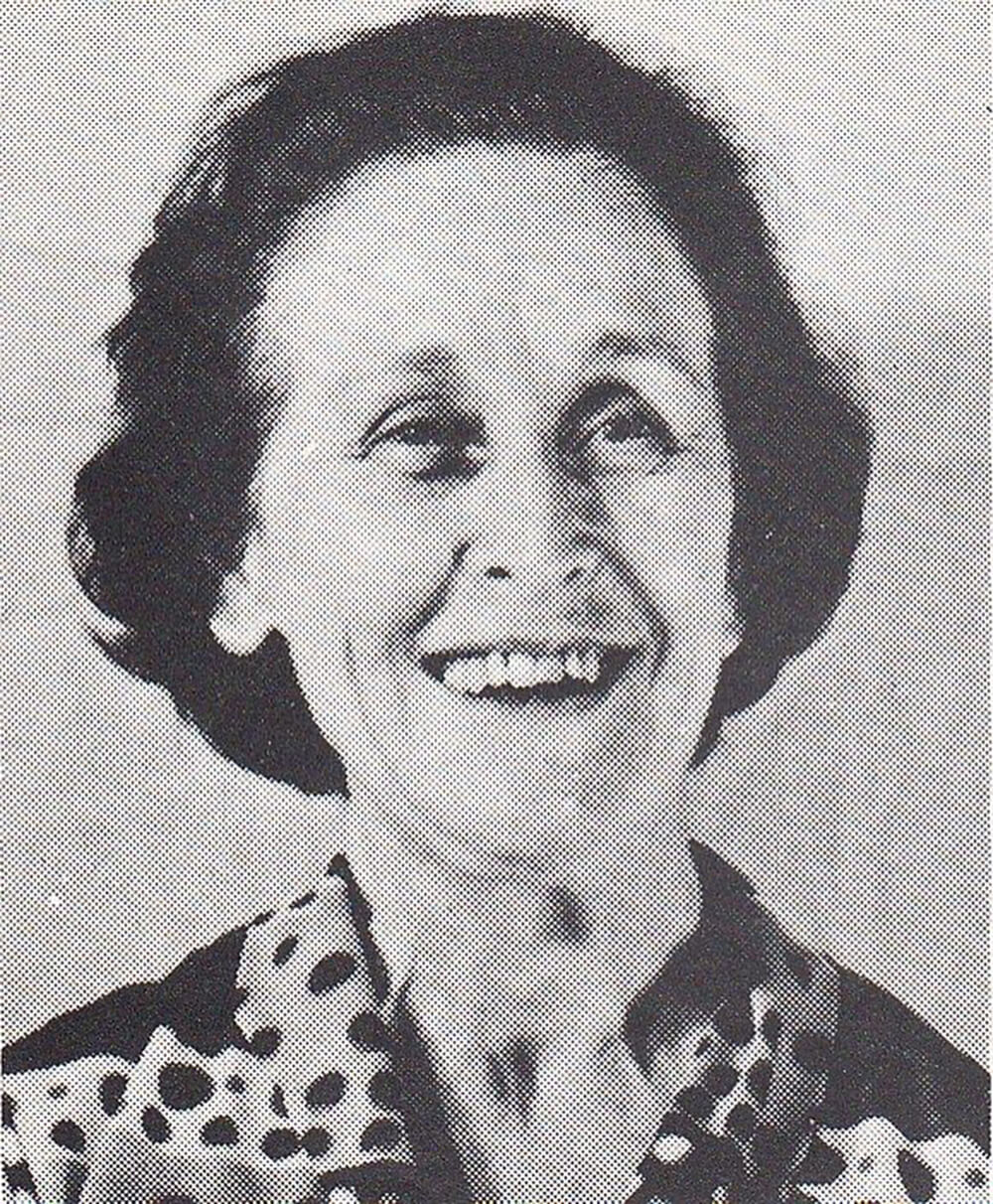 Black and white portrait of a smiling woman with short wavy hair wearing a patterned top.