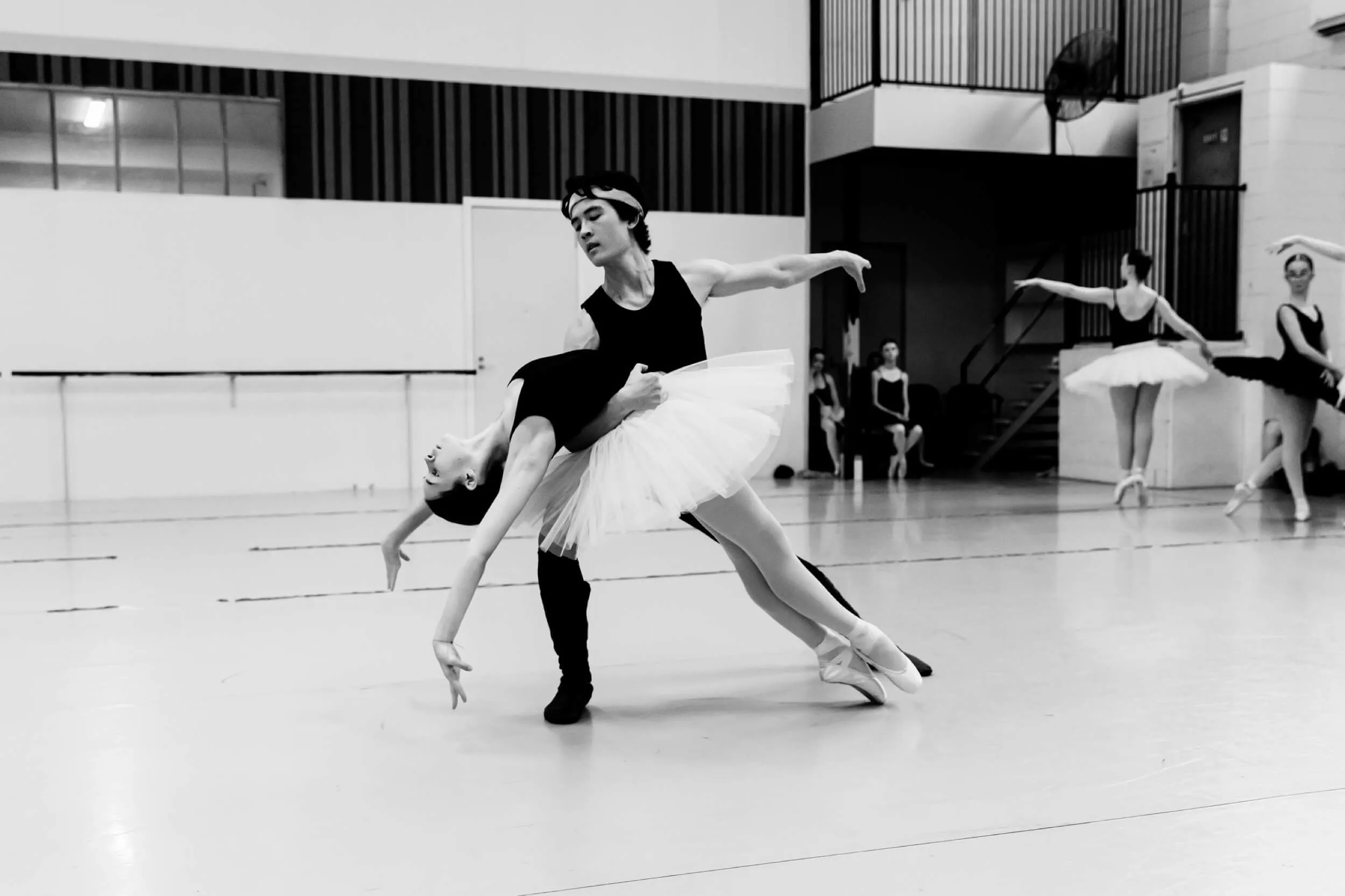 Male ballet dancer supporting female dancer in a deep backbend during rehearsal in a studio.