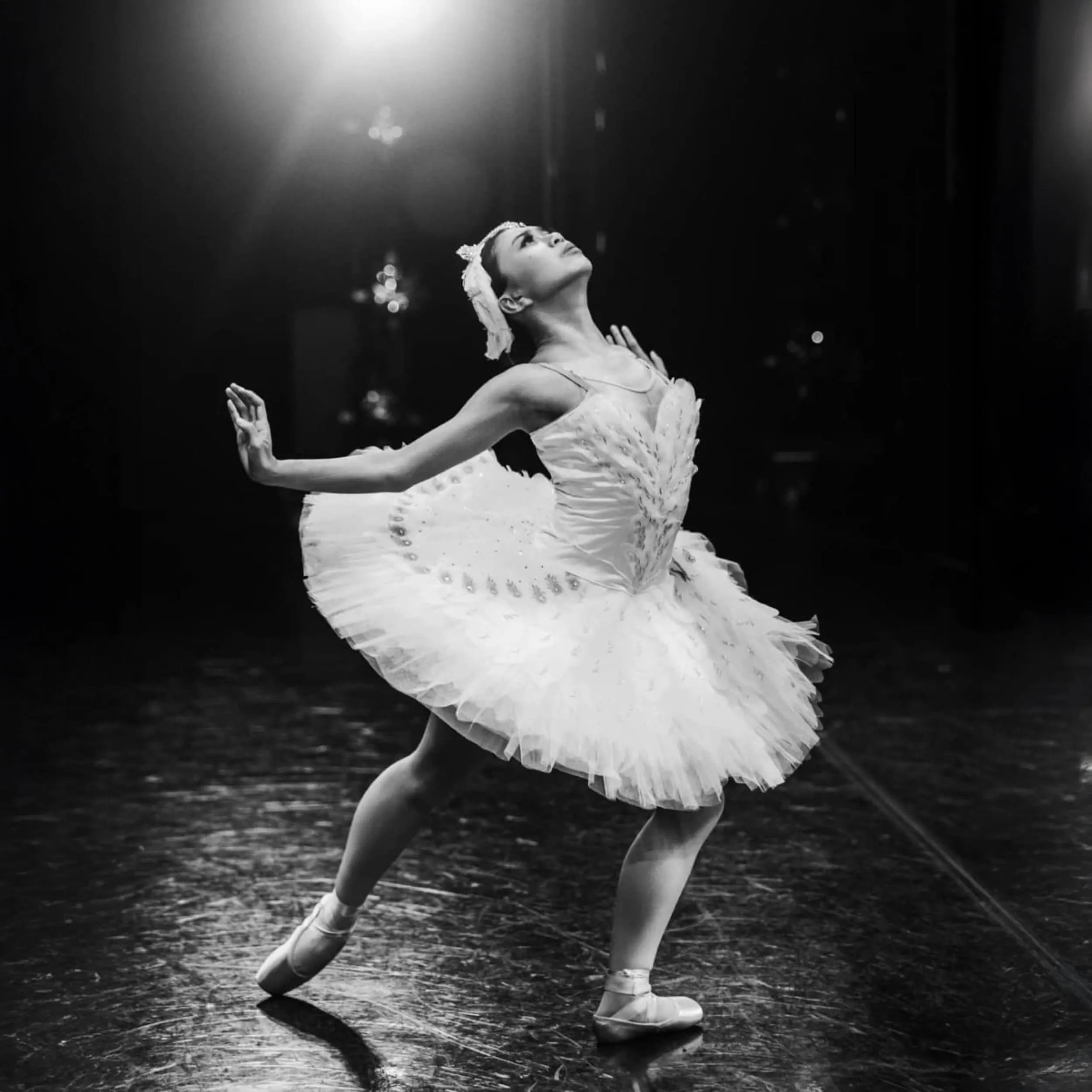 Ballet dancer in white tutu performing on stage in a dramatic pose.