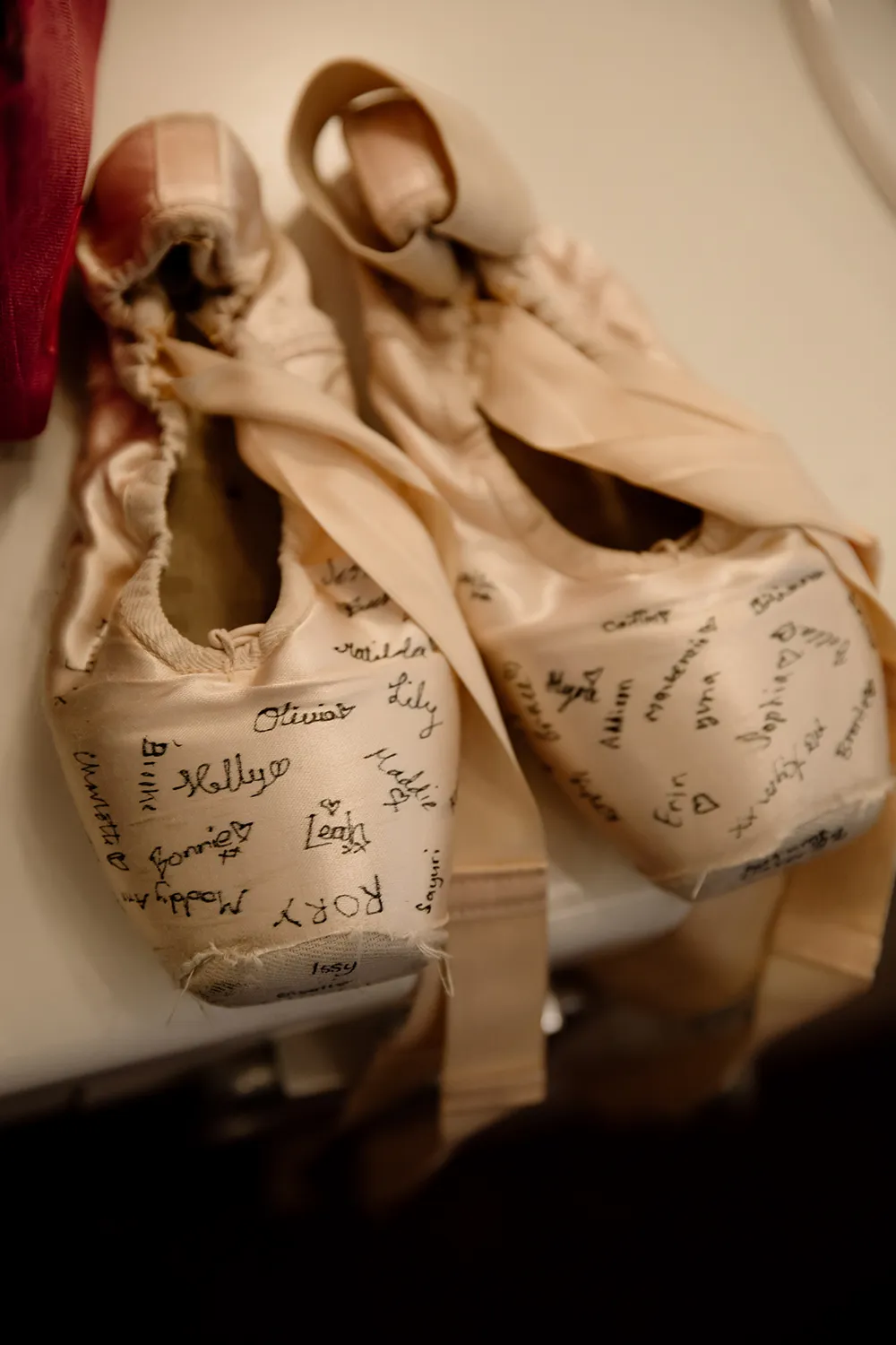 Pair of worn ballet pointe shoes resting on a surface, covered in handwritten names and small hearts.
