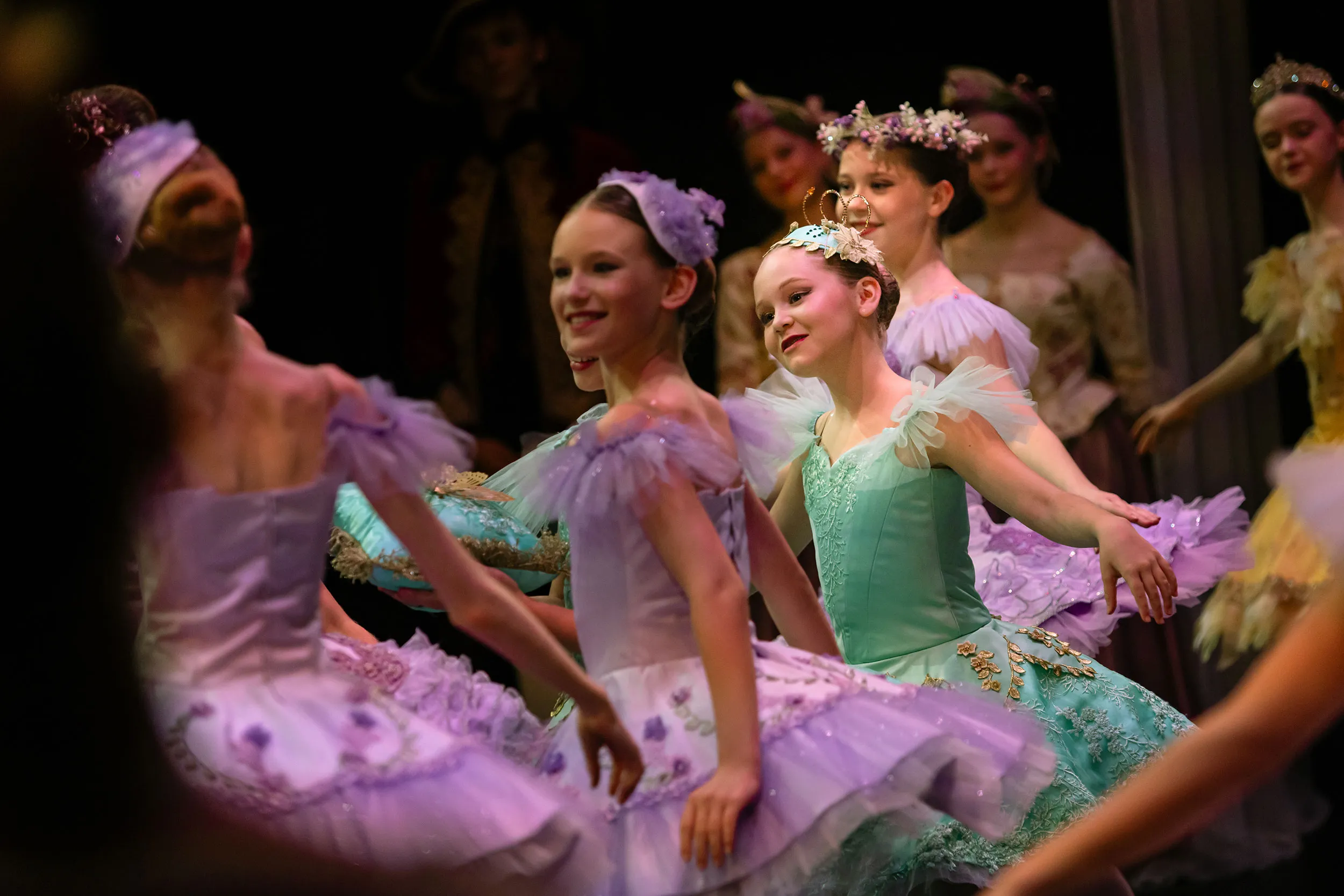 Young ballerinas in colorful tutus performing a ballet on stage, smiling and dancing gracefully.