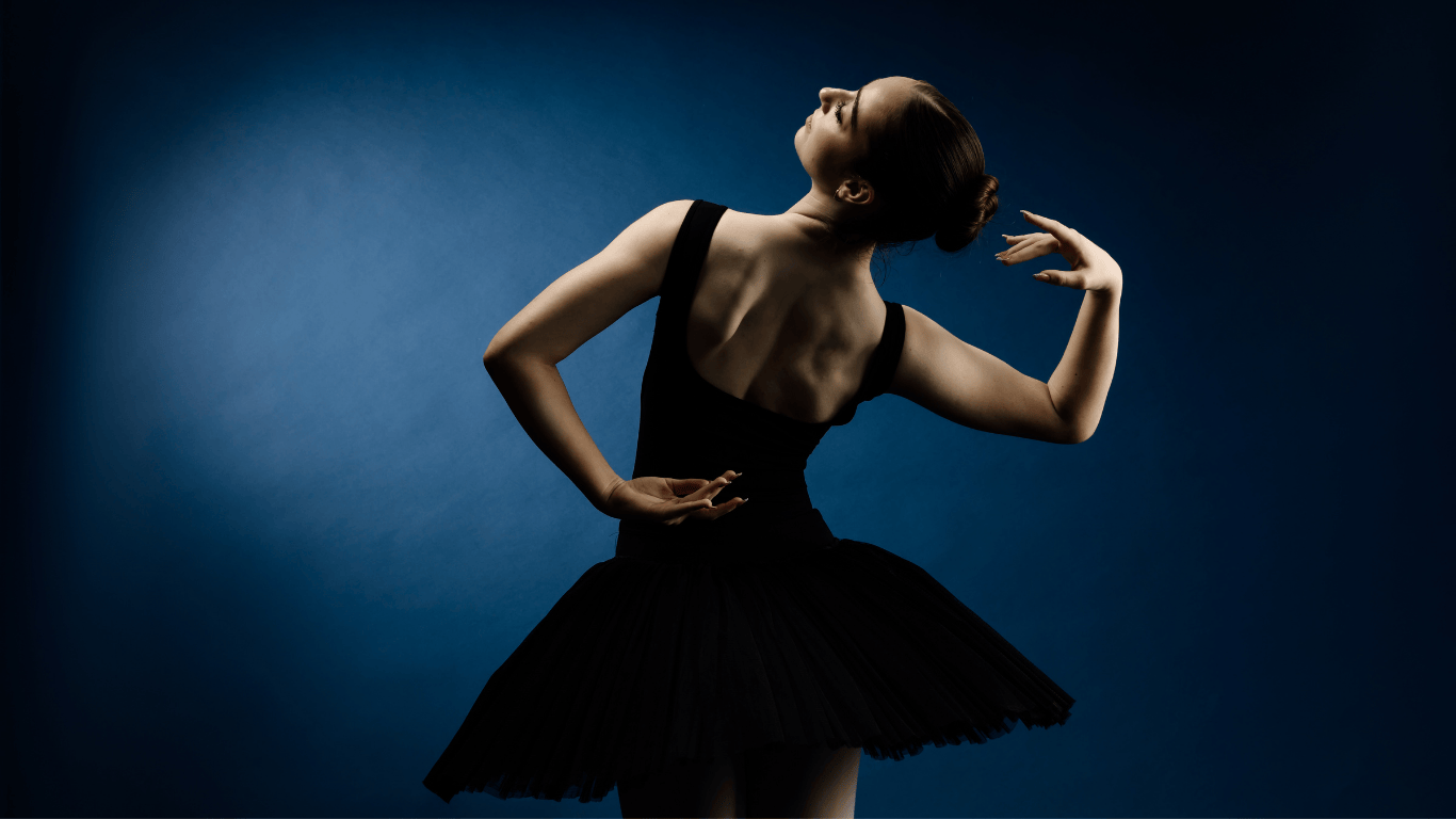 Ballet dancer in a black tutu striking an elegant pose against a dark blue background.
