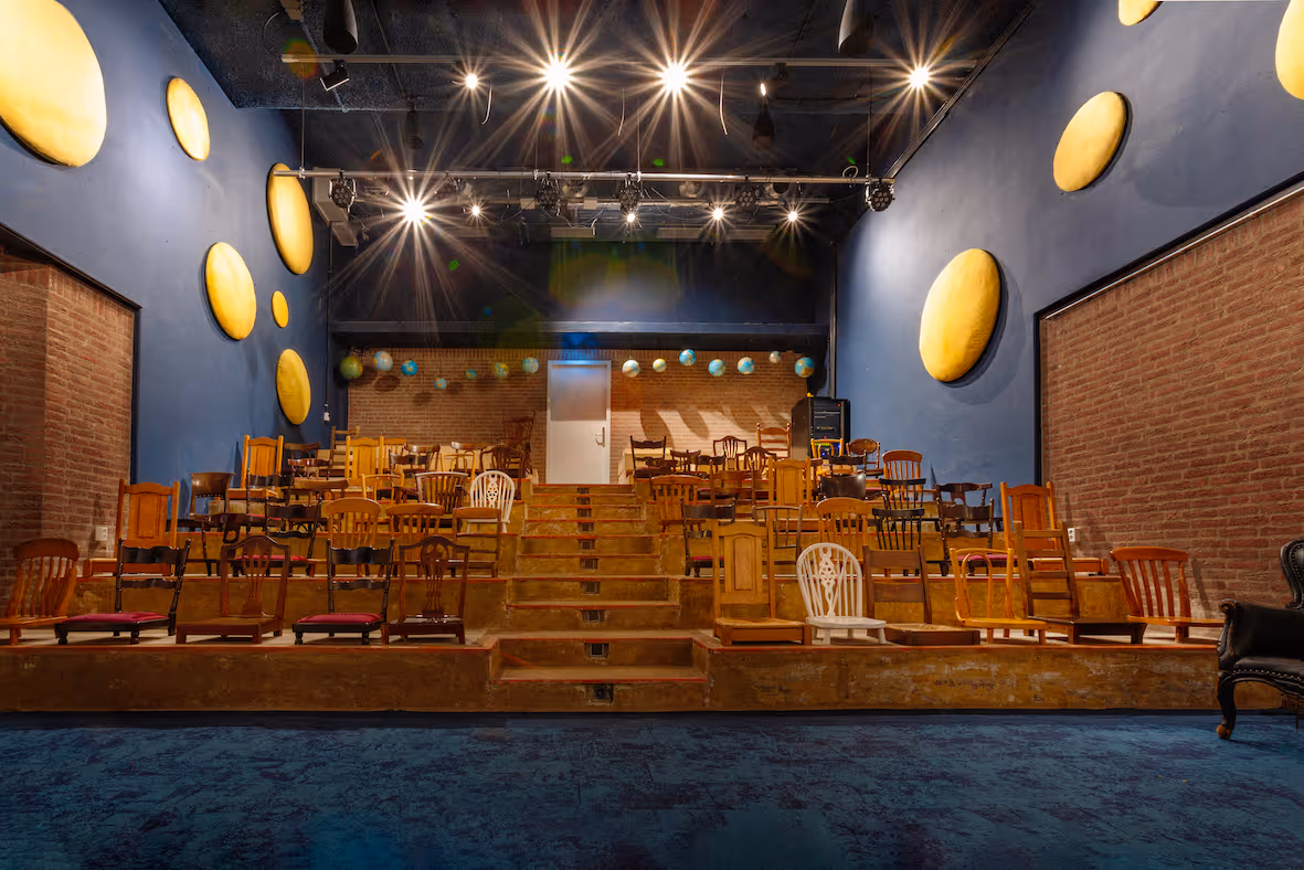 Collegezaal met diverse vintage stoelen op houten tribunes en muren met blauwe en bakstenen afwerking met grote gele cirkels.