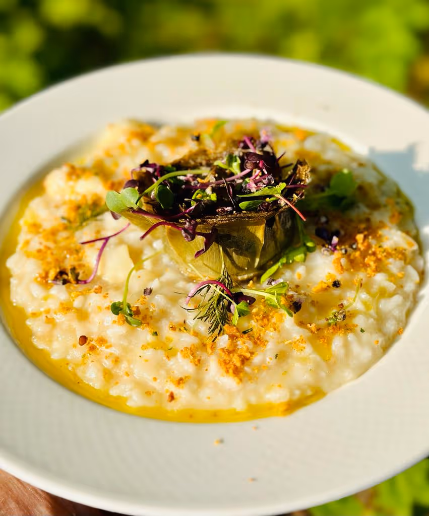 Romige risotto met een artisjokhart en verse kruiden op een wit bord.