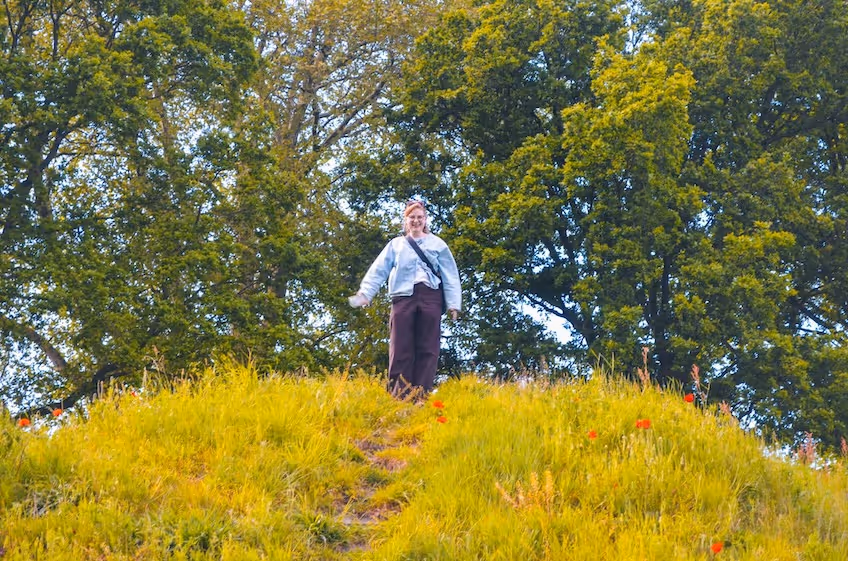Vrouw staat bovenop een grasheuvel omringd door groene bomen en bloemen op de Bussumerheide.