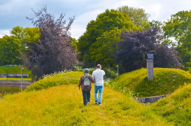 Een stel loopt hand in hand over een grasachtig pad omringd door bomen en struiken bij Naarden Vesting.
