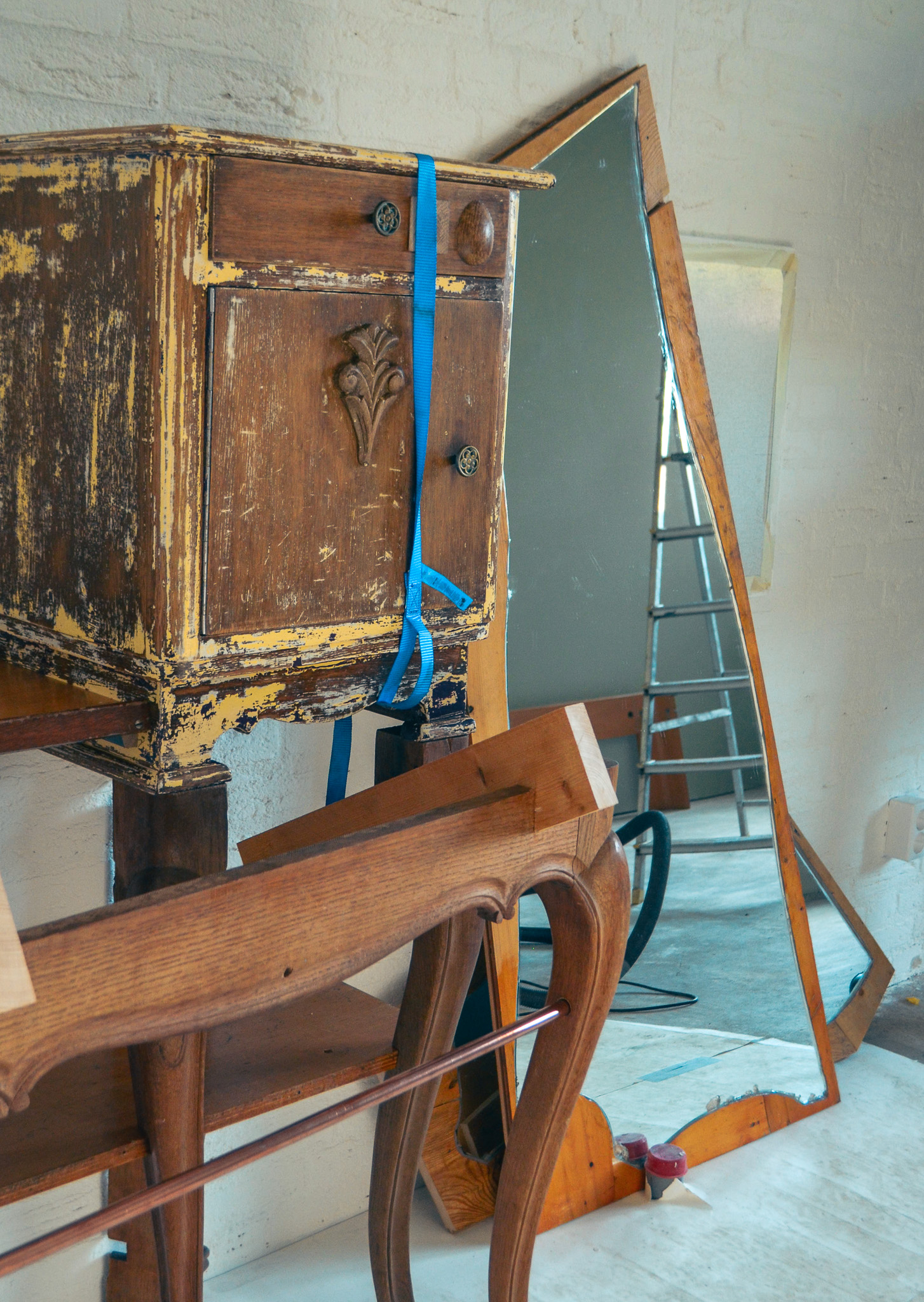 Detail van de nog in aanbouw zijnde hotelkamer "Stukwerk" bij Hotel de Groene Afslag. Vintage houten meubelstukken en een grote spiegel staan tegen een witte muur in de kunstzinnige hotelkamer.