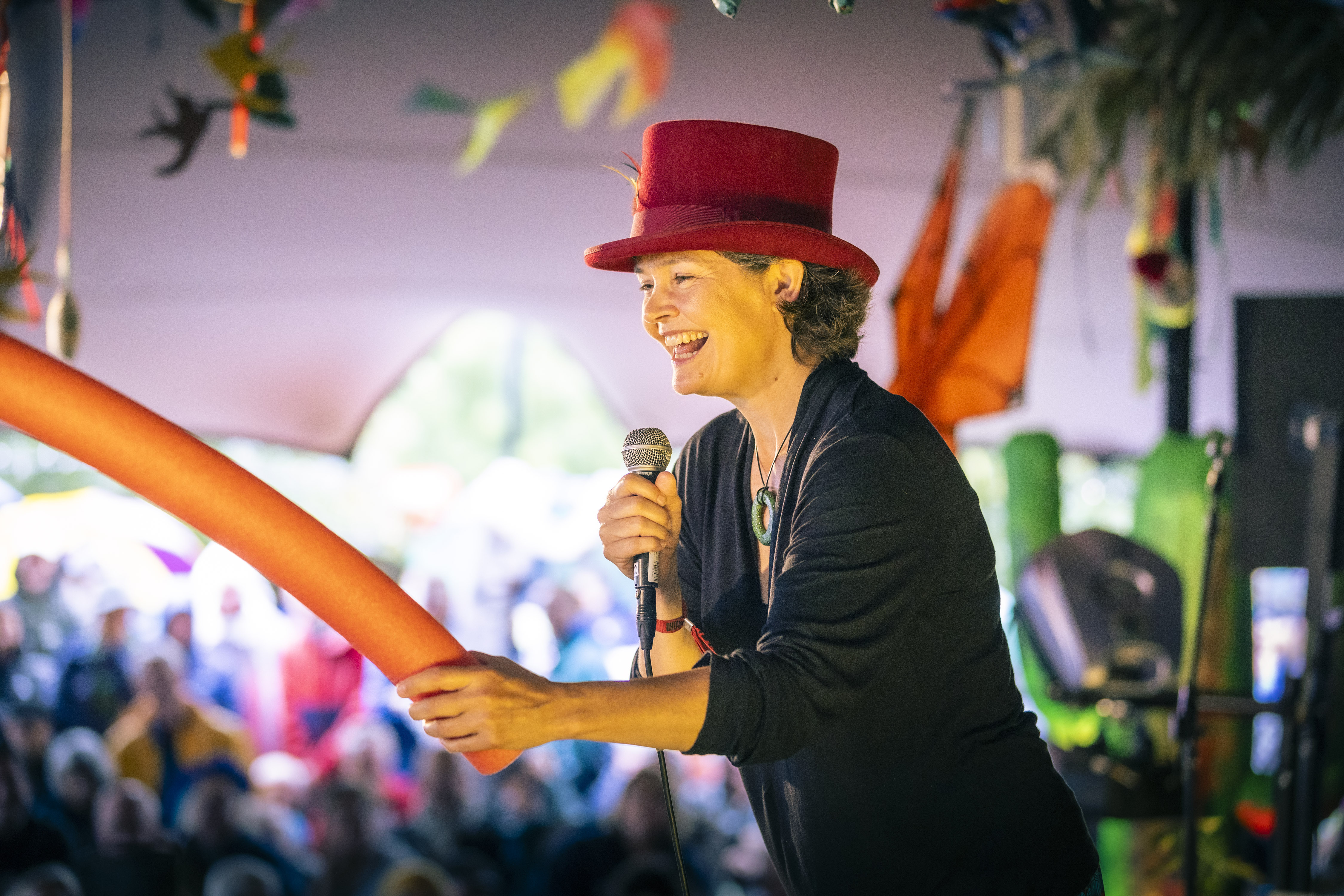Kate Raworth, bedenker van het economische "donut" model, staat lachend op een podium met microfoon in de hand. Op de achtergrond is een luisterend publiek zichtbaar. 