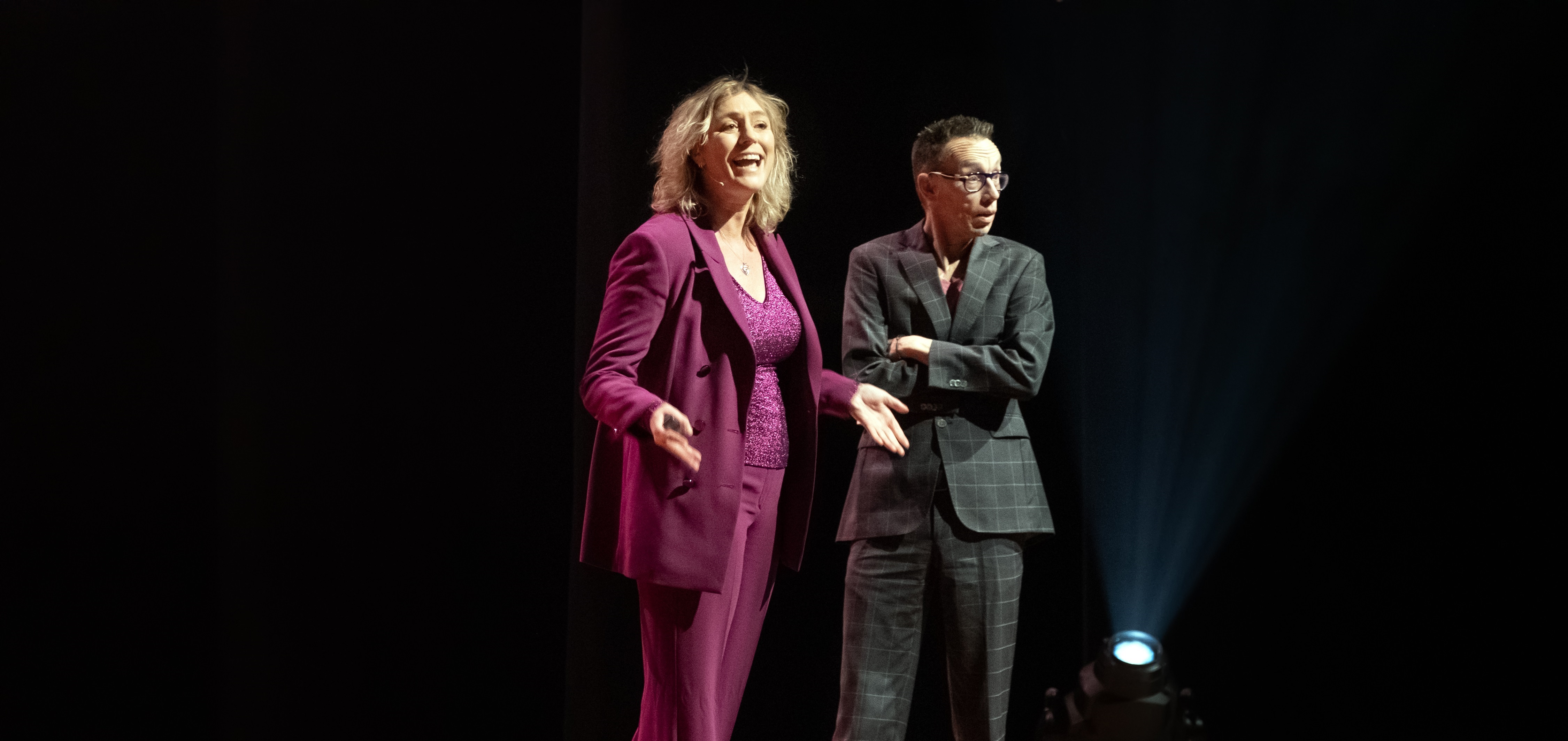 Jitske Kramer, corporate antropoloog, ondernemer en bestsellerauteur staat samen met Dolf Jansen, cabaretier, presentator, columnist en schrijver op een podium te presenteren