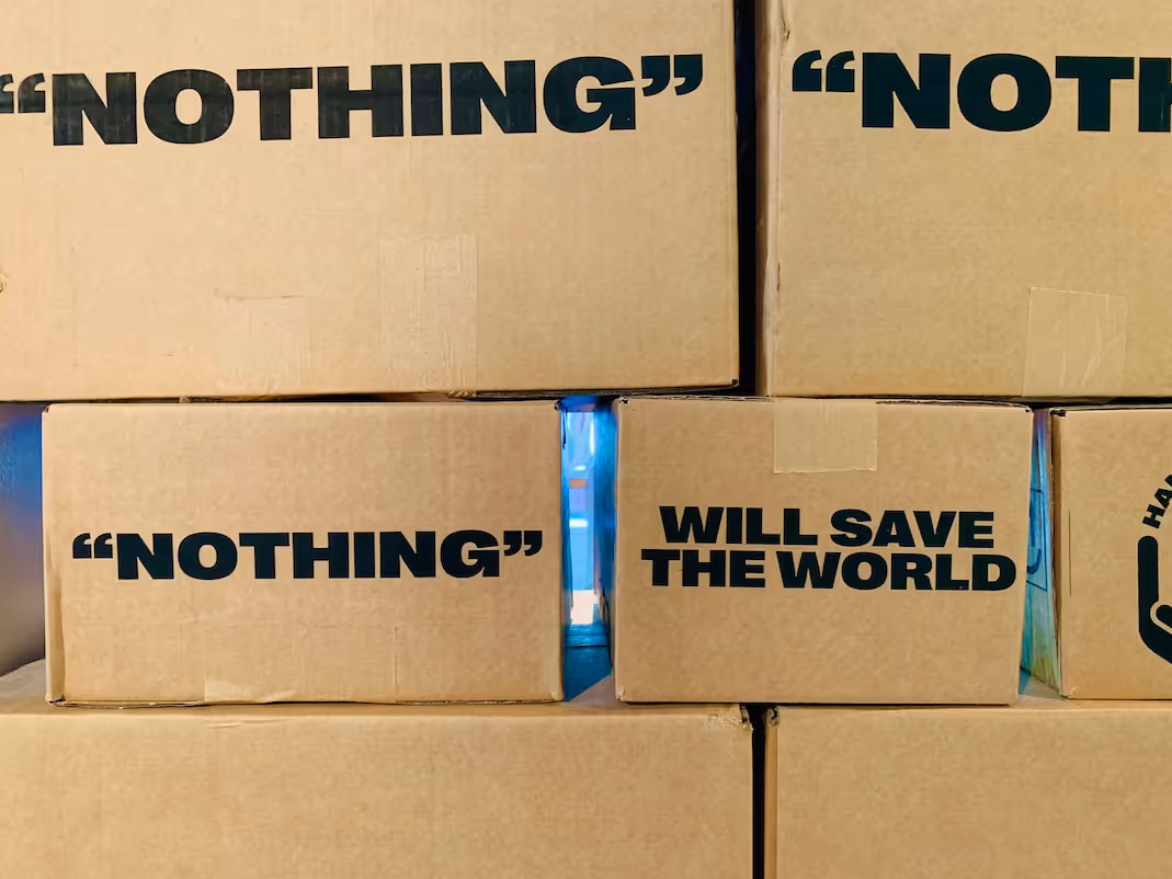 Op elkaar gestapelde kartonnen dozen waarop afwisselend "nothing" tussen aanhalingstekens en "will save the world" staat.