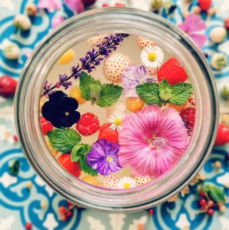 Glas gefermenteerde frisdrank met kleurrijke bloemen en fruit erin. 