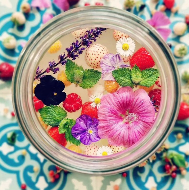 Glas gefermenteerde frisdrank met kleurrijke bloemen en fruit erin.