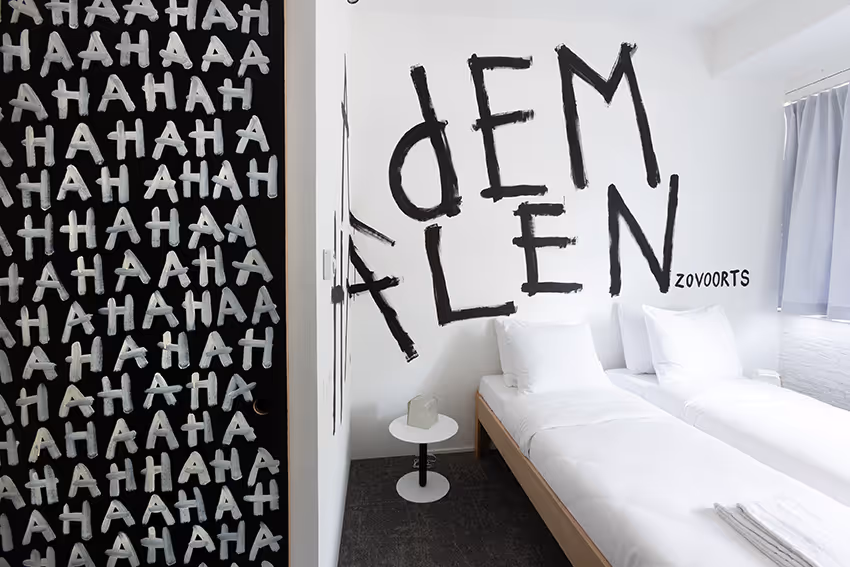 Kunstzinnige hotelkamer "Hahahaha" in het hotel van De Groene Afslag, ontworpen door Rogier Roeters. Op de witte muur boven het bed is in grote zwarte letters "Ademhalen enzovoorts" geschilderd