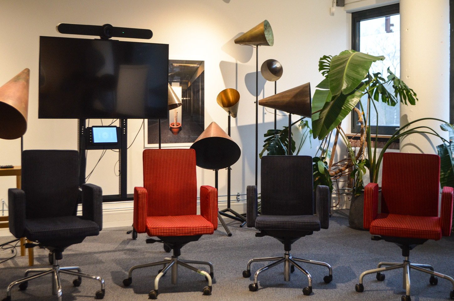 Vergaderruimte De Roeptoeter bij De Groene Afslag. Vier gekleurde bureaustoelen met op de achtergrond een beeldscherm, planten en metalen roeptoeters op standaarden.
