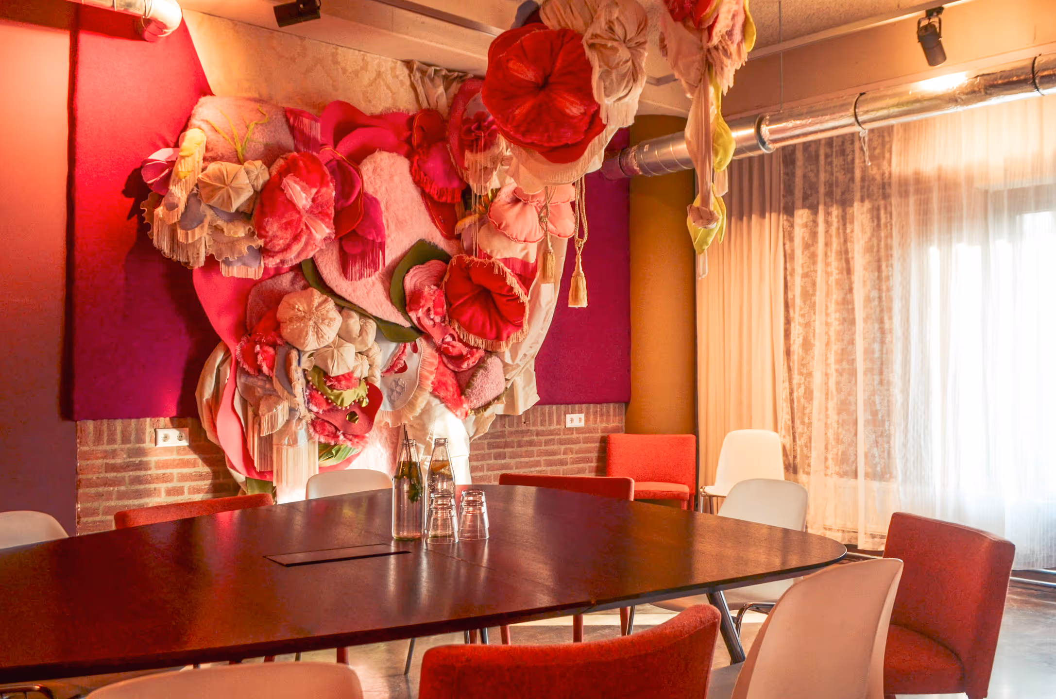 Detail een abstract driedimensionaal kunstwerk van zachte textiel met meerdere kleuren en structuren, at aan de muur hangt in De Fijne Kamer van het Ongemak bij De Groene Afslag.