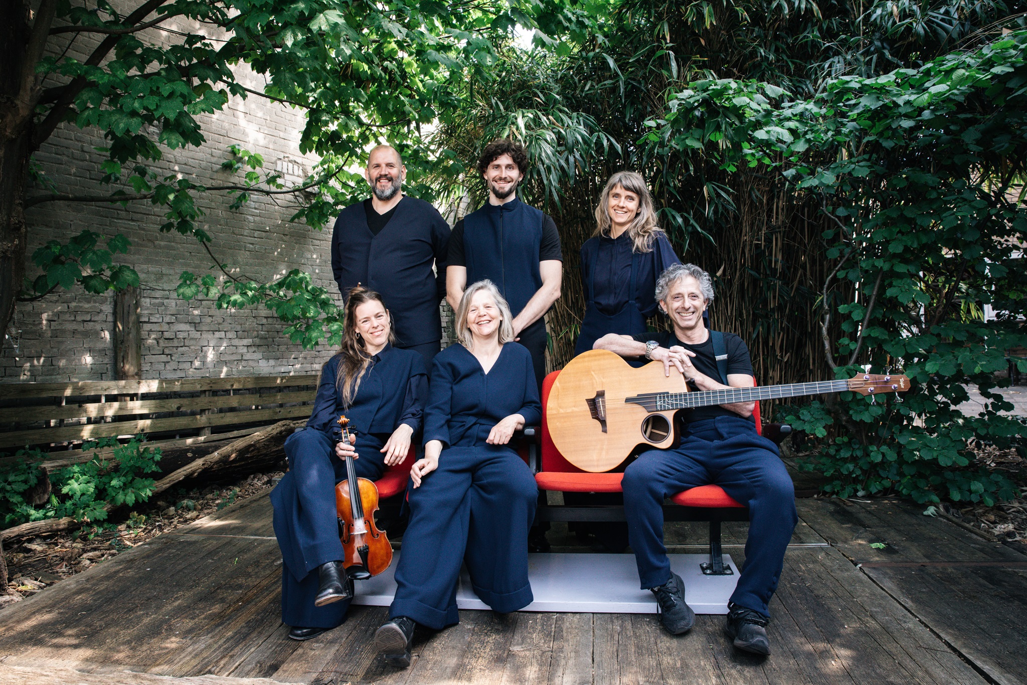 Zes leden van Theater Draad poseren in een tuin met muziekinstrumenten in hun hand