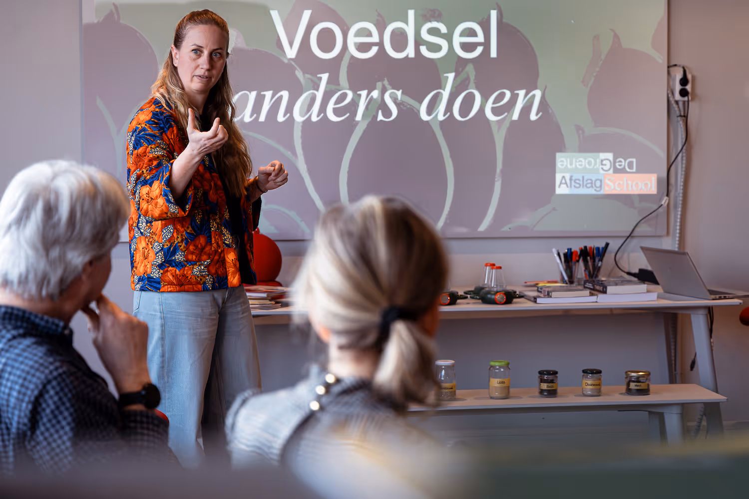 Lerares van cursus voedsel anders doen voor een presentatie terwijl cursisten luisteren.