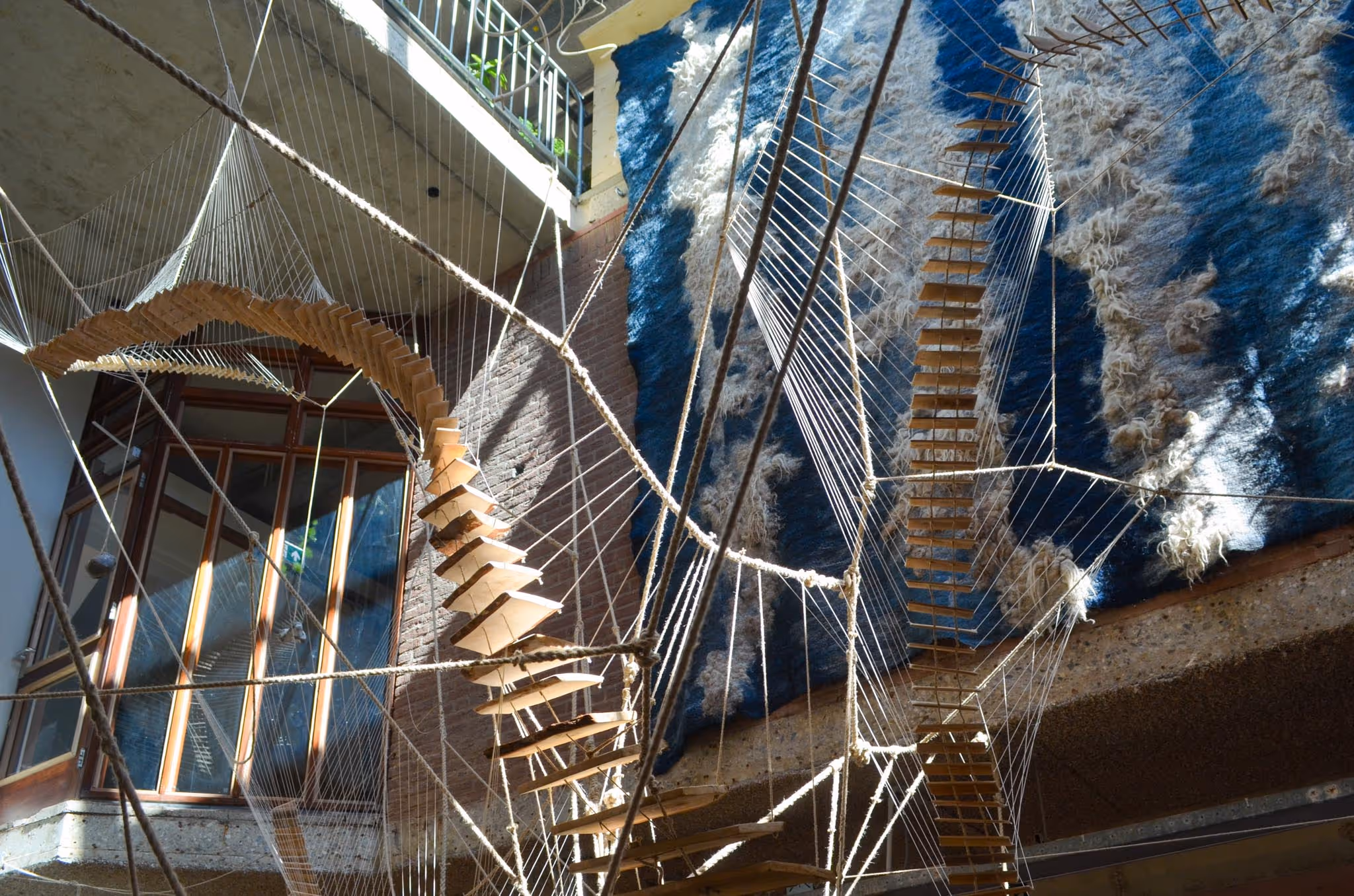 Kunstige trap die tot hoog in een ruimte rijkt met op de achtergrond een blauw wandkleed. 