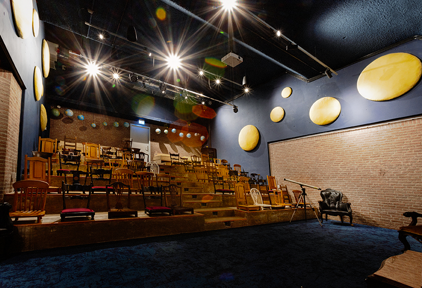 Collegezaal met houten stoelen en donker blauwe muren. 