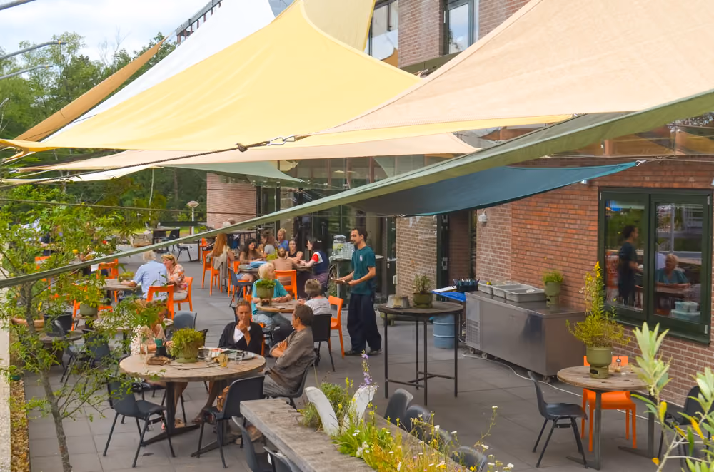 Terras met mensen aan de tafels en zeilen er boven als zonnewering