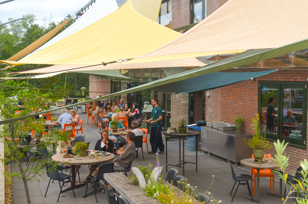 Terras met mensen aan de tafels en zeilen er boven als zonnewering