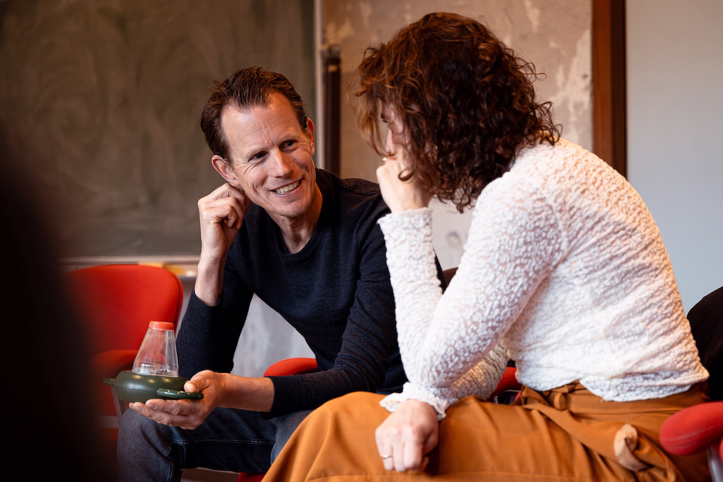Een man en vrouw zitten glimlachend met elkaar te praten in een klaslokaal.