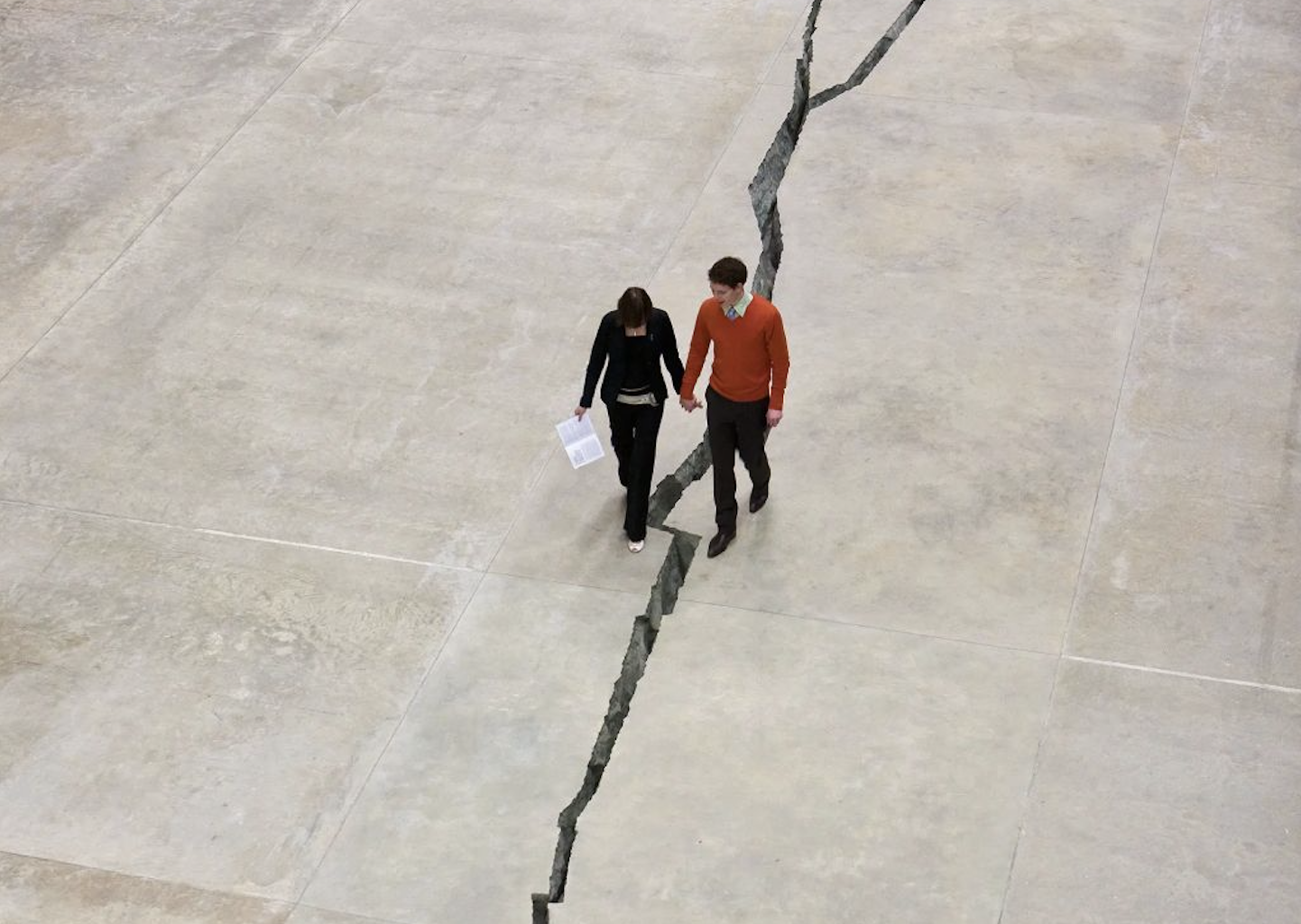 Twee mensen die over een grote scheur in een betonnen vloer lopen