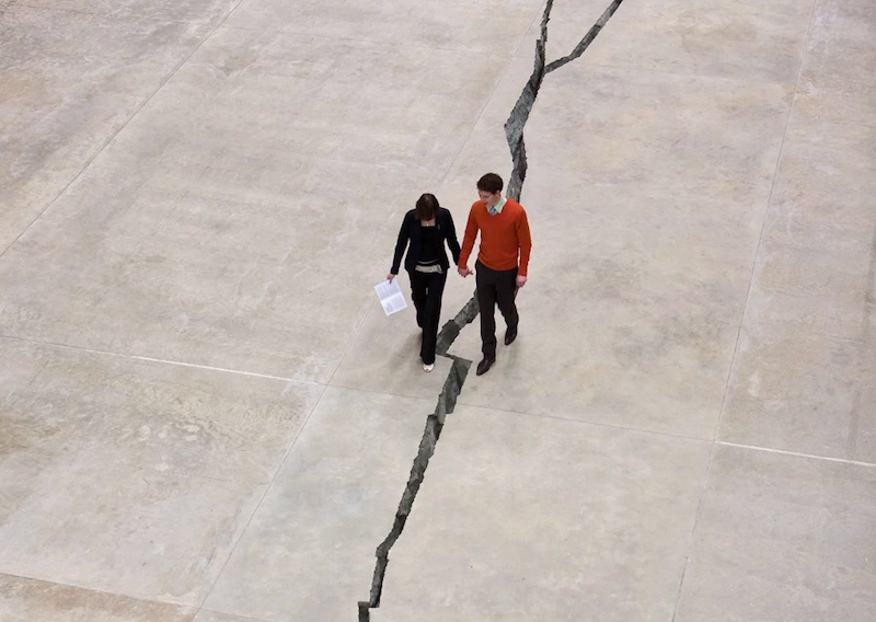 Twee mensen die over een grote scheur in een betonnen vloer lopen