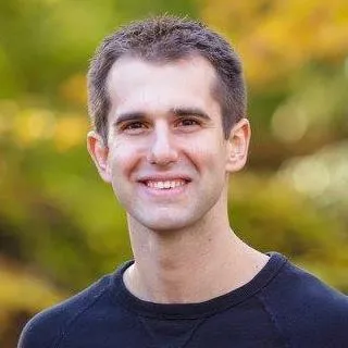 Young man smiling outdoors in a black shirt with a blurred background of autumn-colored trees — client of Colorado Wealth Group