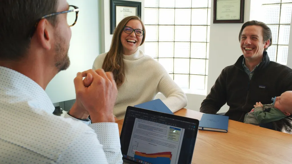 Young couple with baby meeting a financial advisor in a bright office, smiling while reviewing personalized financial strategies—highlighting Colorado Wealth Group’s family-focused wealth planning services