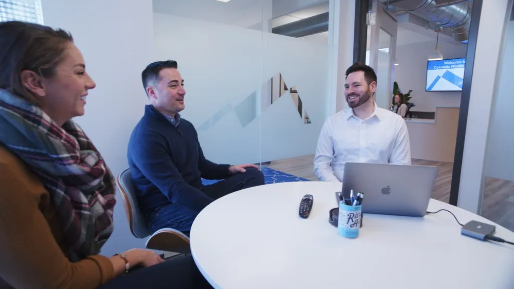 Financial advisor meeting with a smiling couple in a modern Colorado Wealth Group office, reflecting a welcoming and personalized wealth management experience in Denver, CO