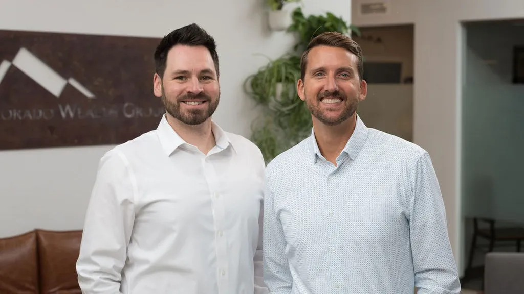 Two smiling financial advisors standing inside the Colorado Wealth Group office, representing the friendly and professional leadership team dedicated to personalized financial planning in Denver, CO