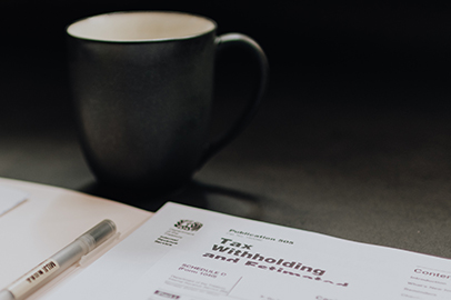 IRS tax withholding and estimated payment documents on a desk with a coffee mug and pen, representing detailed tax planning services by Colorado Wealth Group