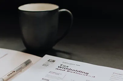 IRS tax withholding and estimated payment documents on a desk with a coffee mug and pen, representing detailed tax planning services by Colorado Wealth Group