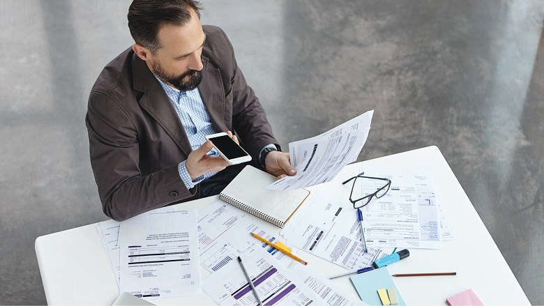 Man reviewing tax forms and financial statements at a desk with a smartphone and notebook, highlighting comprehensive tax planning and wealth advisory services at Colorado Wealth Group