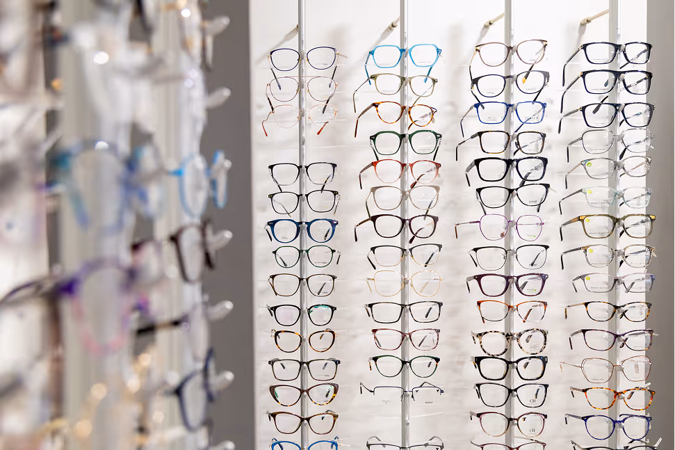 Multiple rows of eyeglasses displayed on white wall in optical store