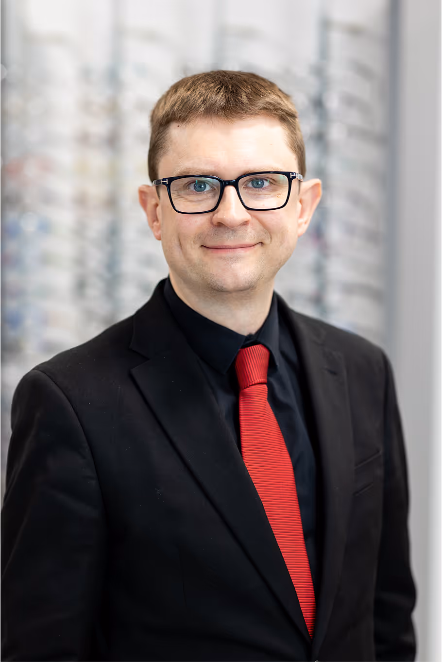 Professional portrait of a man in black suit and red tie wearing glasses