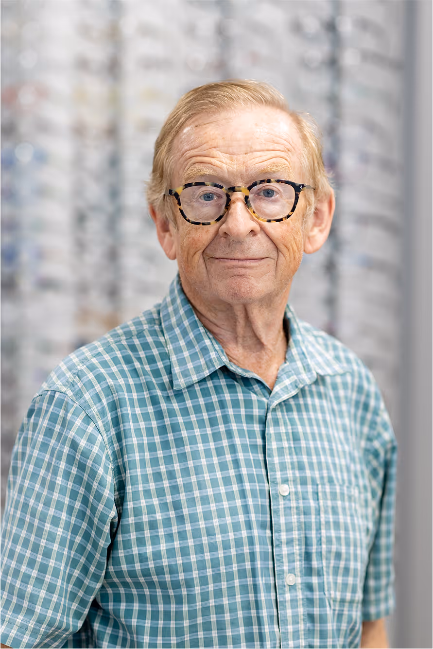 Older gentleman in glasses and blue checkered shirt smiling softly