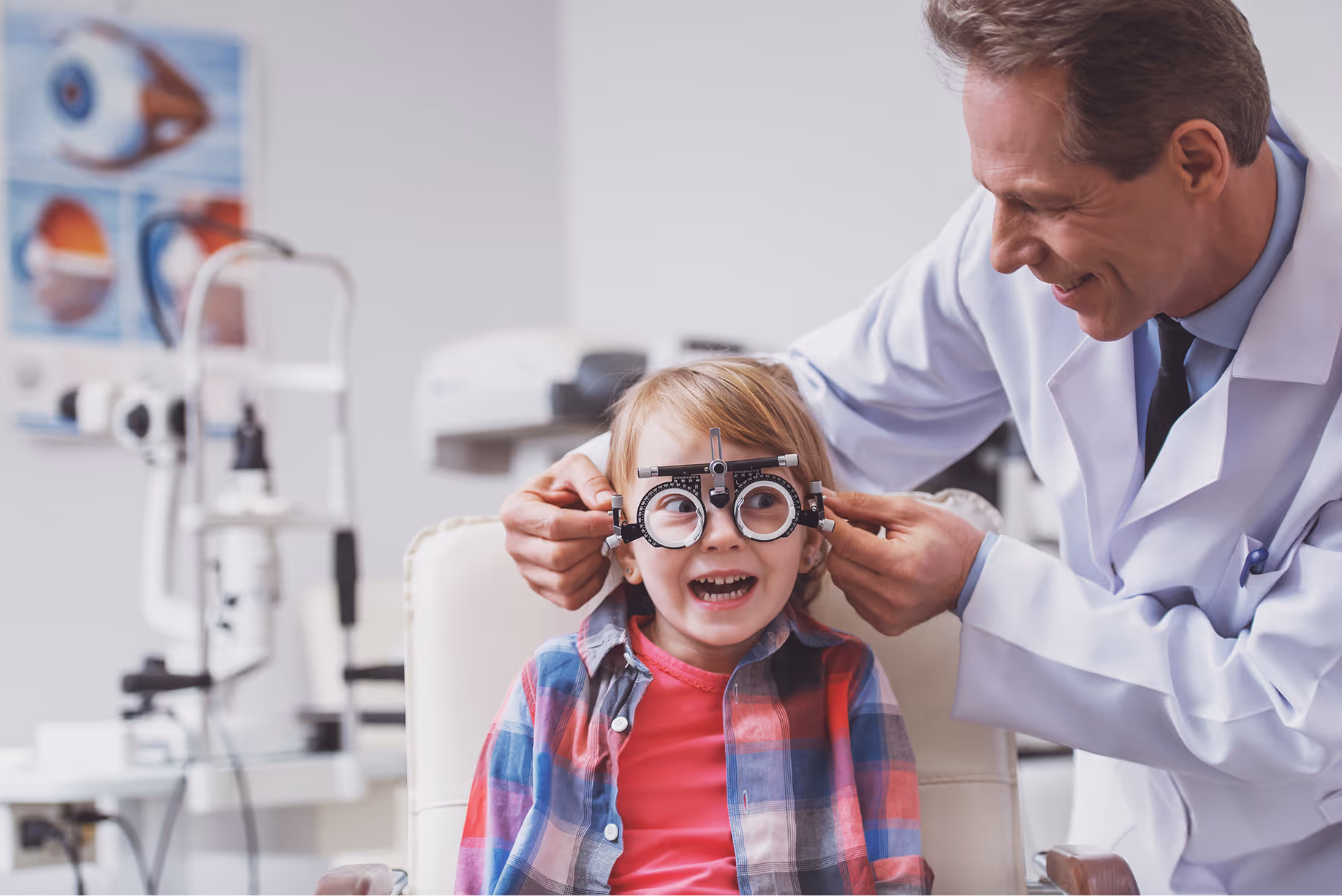 Smiling child getting eye exam with optometrist adjusting trial frames