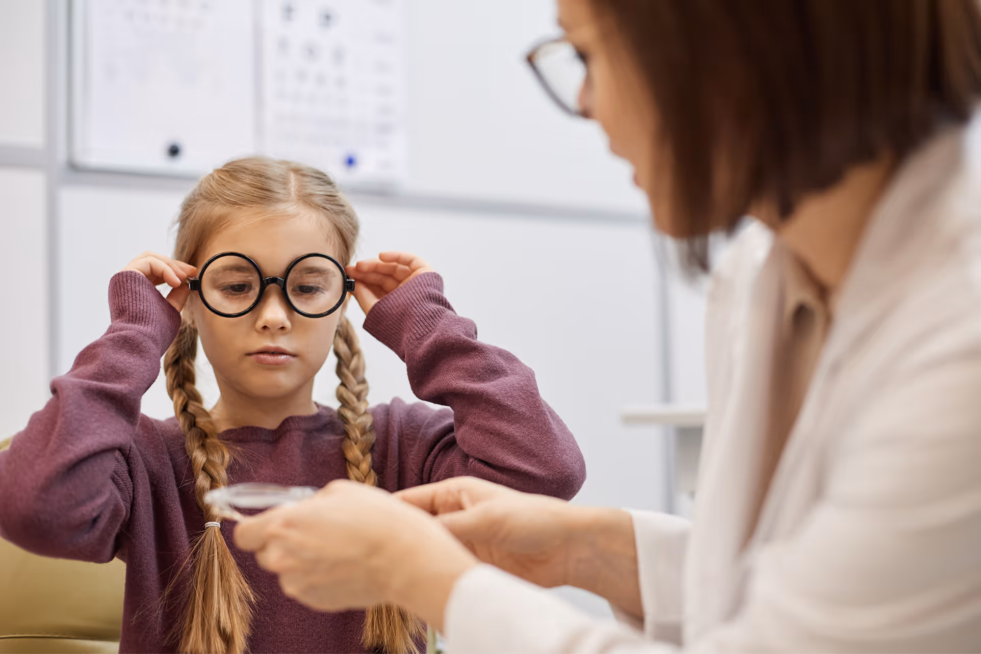 Child with braids trying on glasses during eye exam with professional