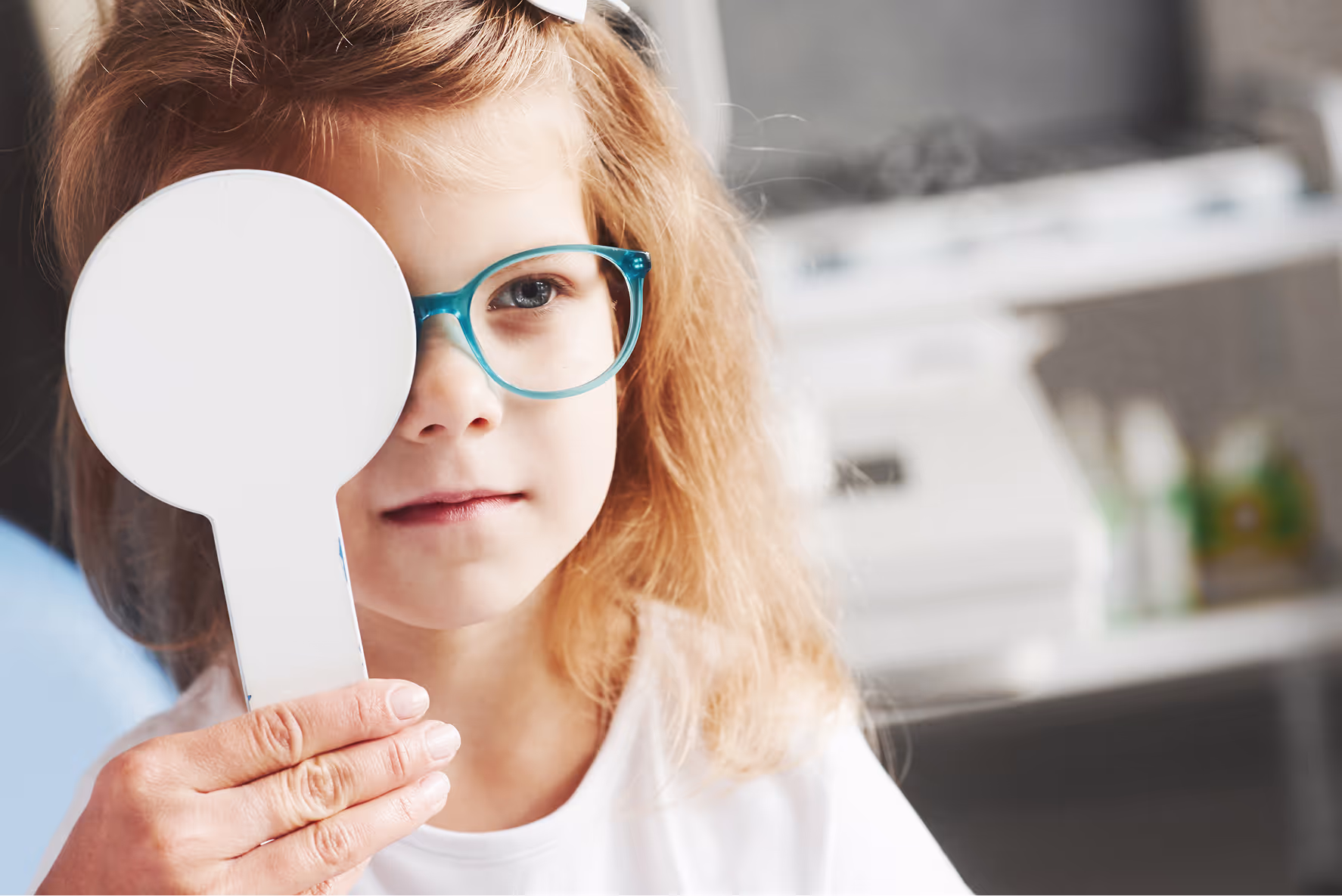 Child with glasses covering one eye during eye exam or vision test