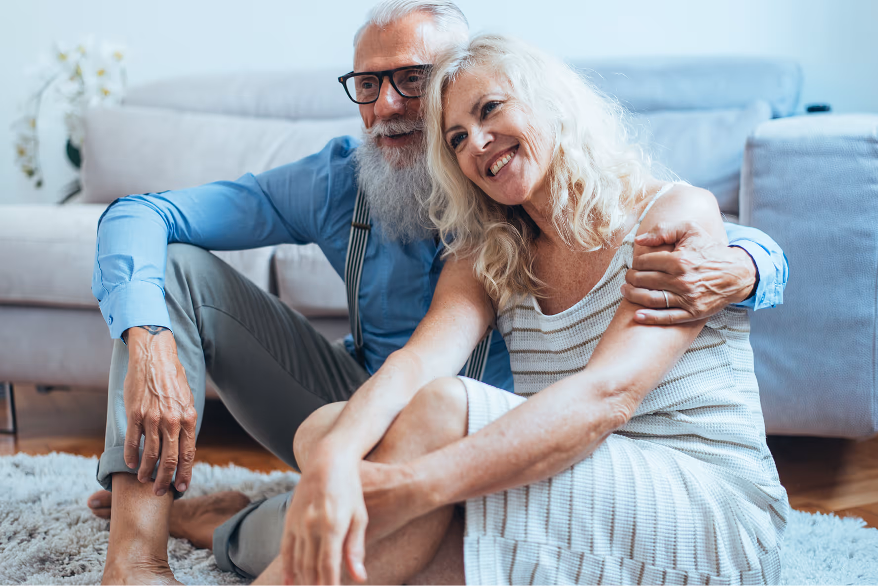 Older couple smiling and embracing, sitting together on floor at home