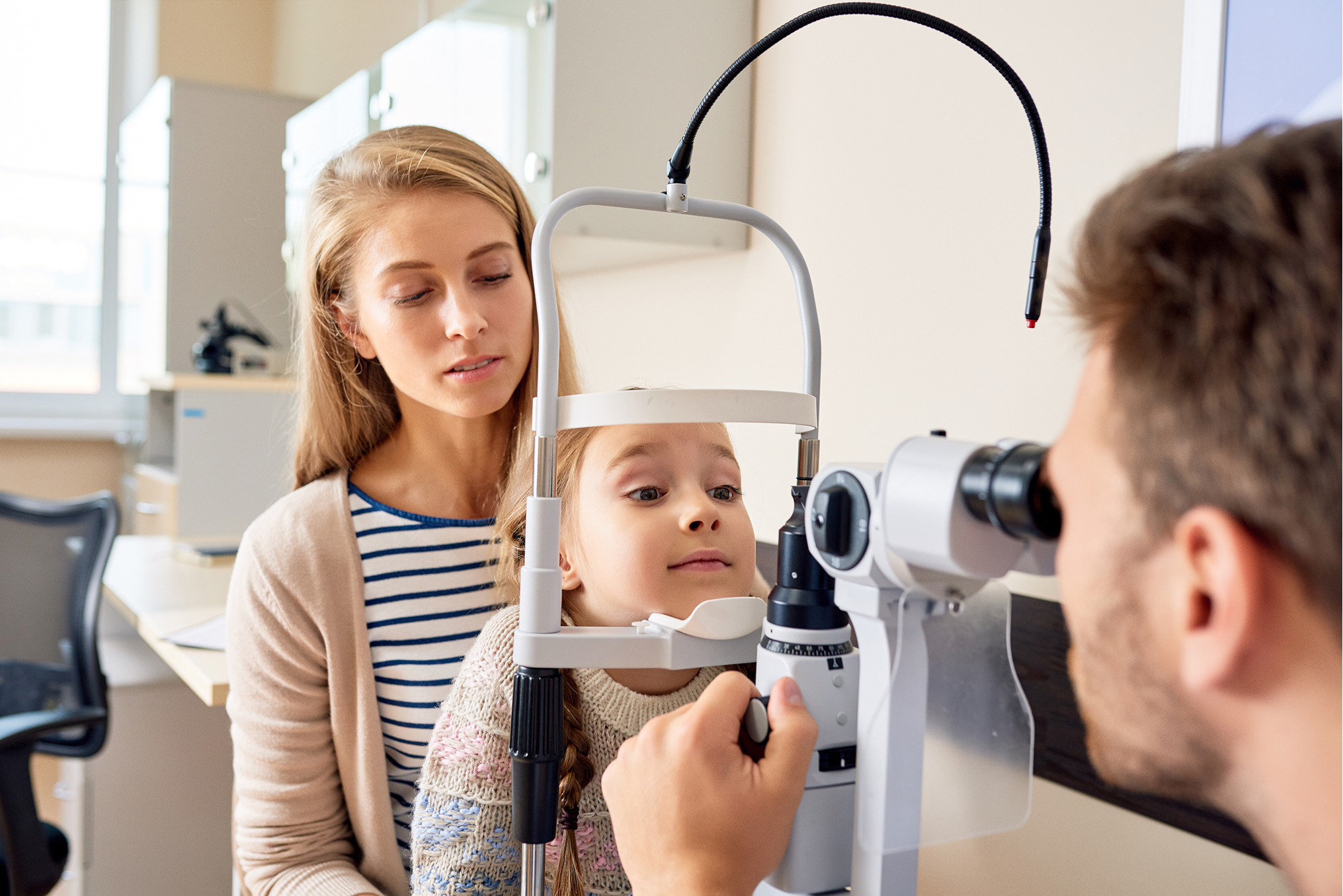 Child receiving eye exam with mother beside slit lamp diagnostic equipment