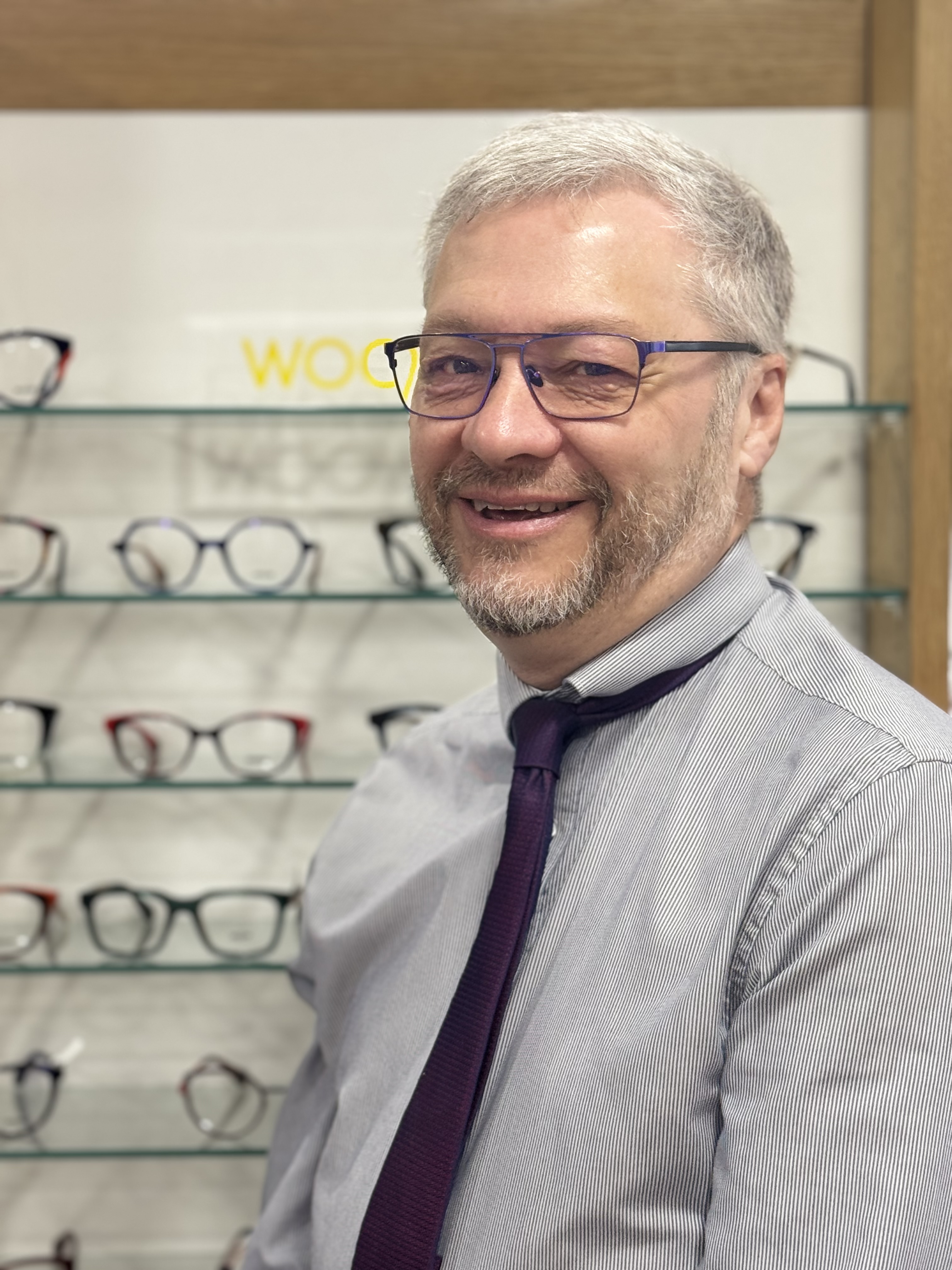 Smiling optician standing in front of eyeglass display shelves