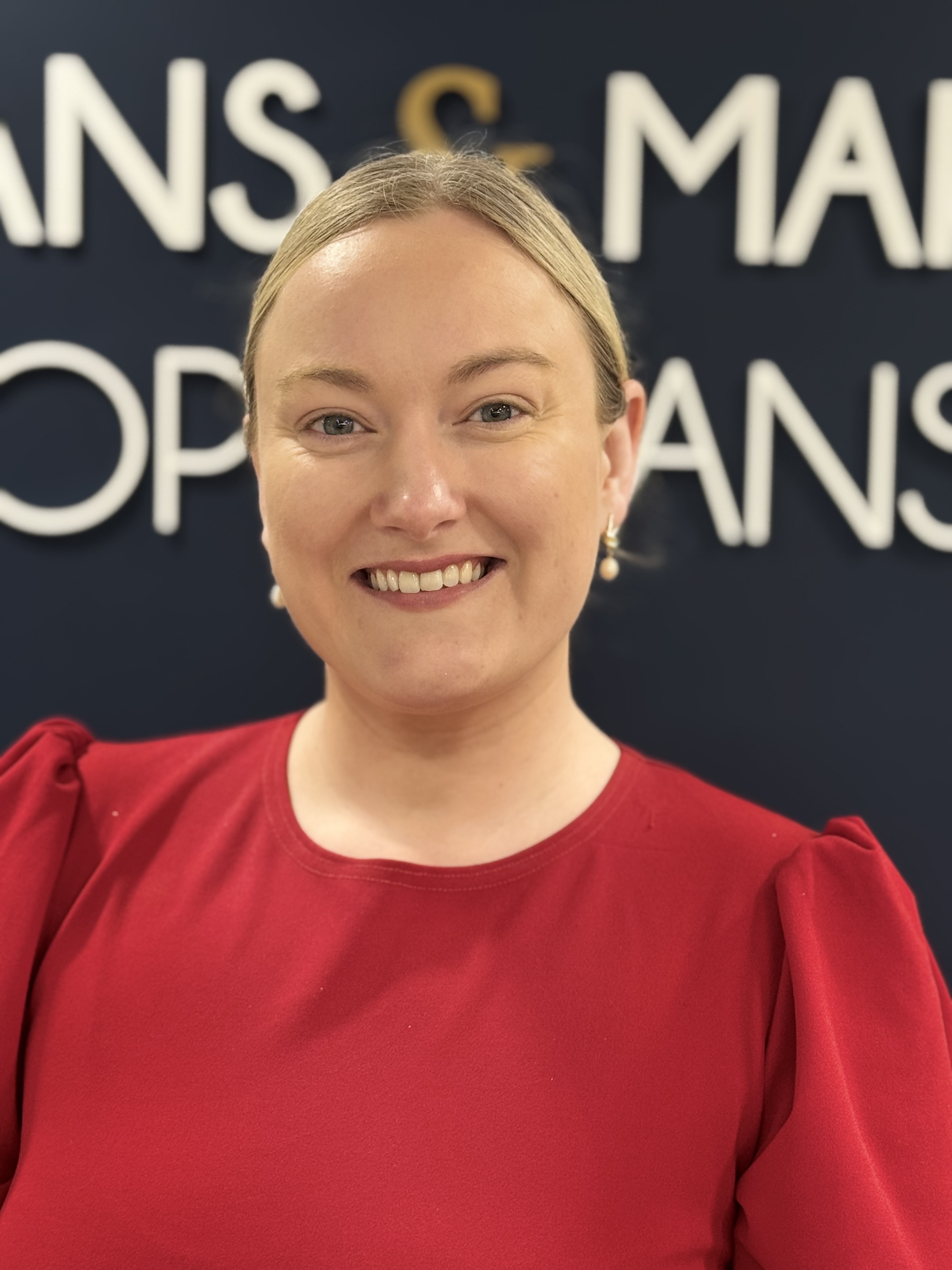 Smiling professional in red top standing in front of corporate signage