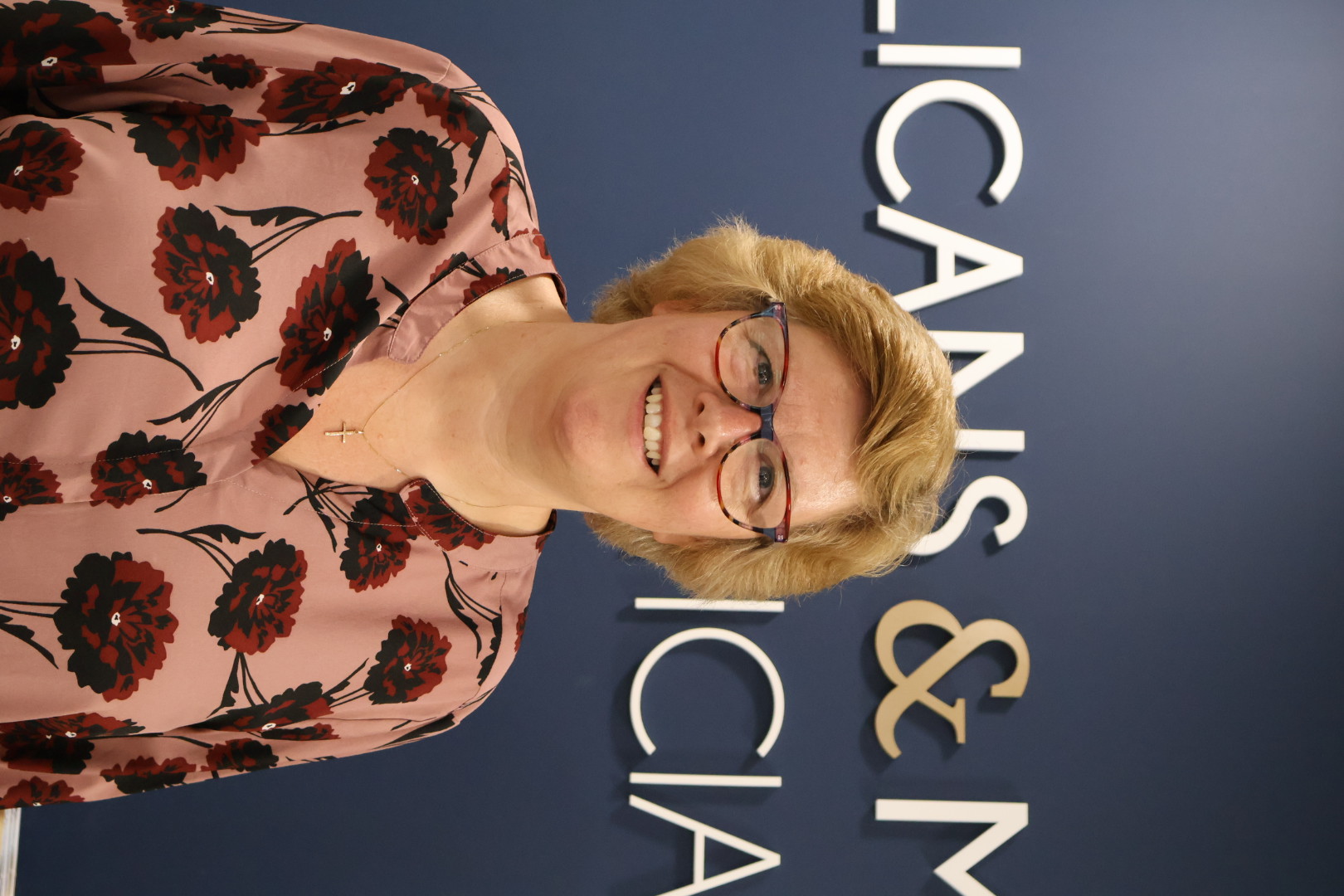 Smiling woman in floral blouse standing in front of professional signage