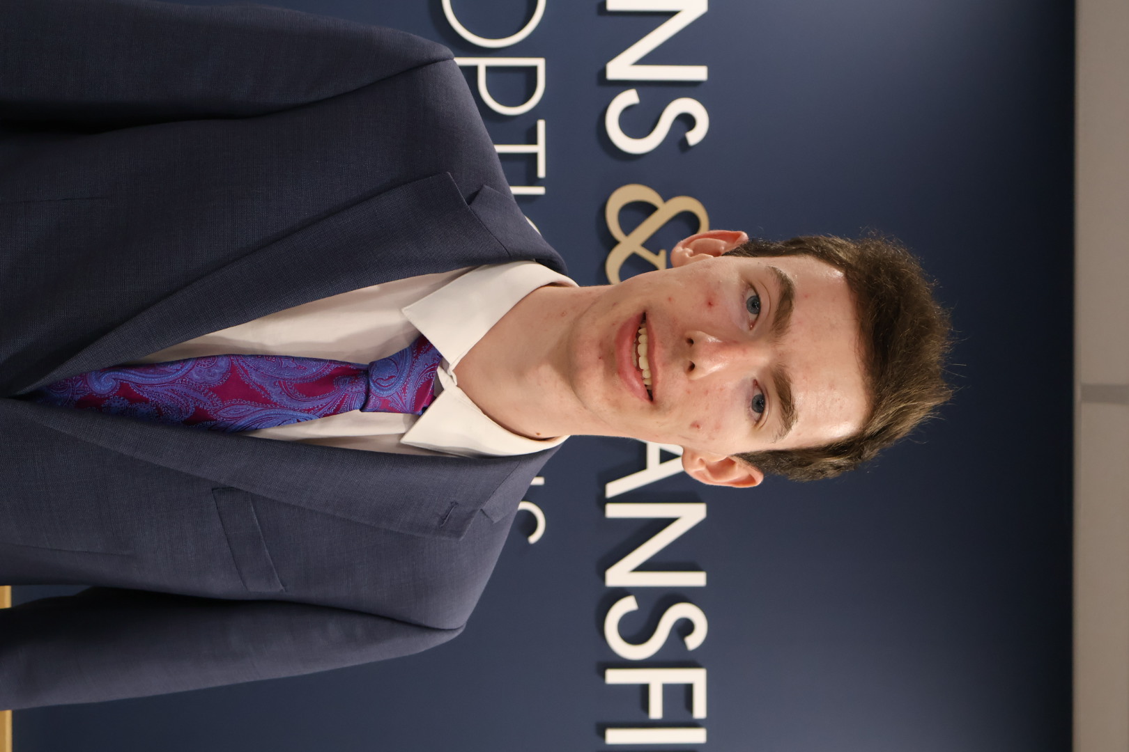 Young professional in gray suit and purple paisley tie smiling