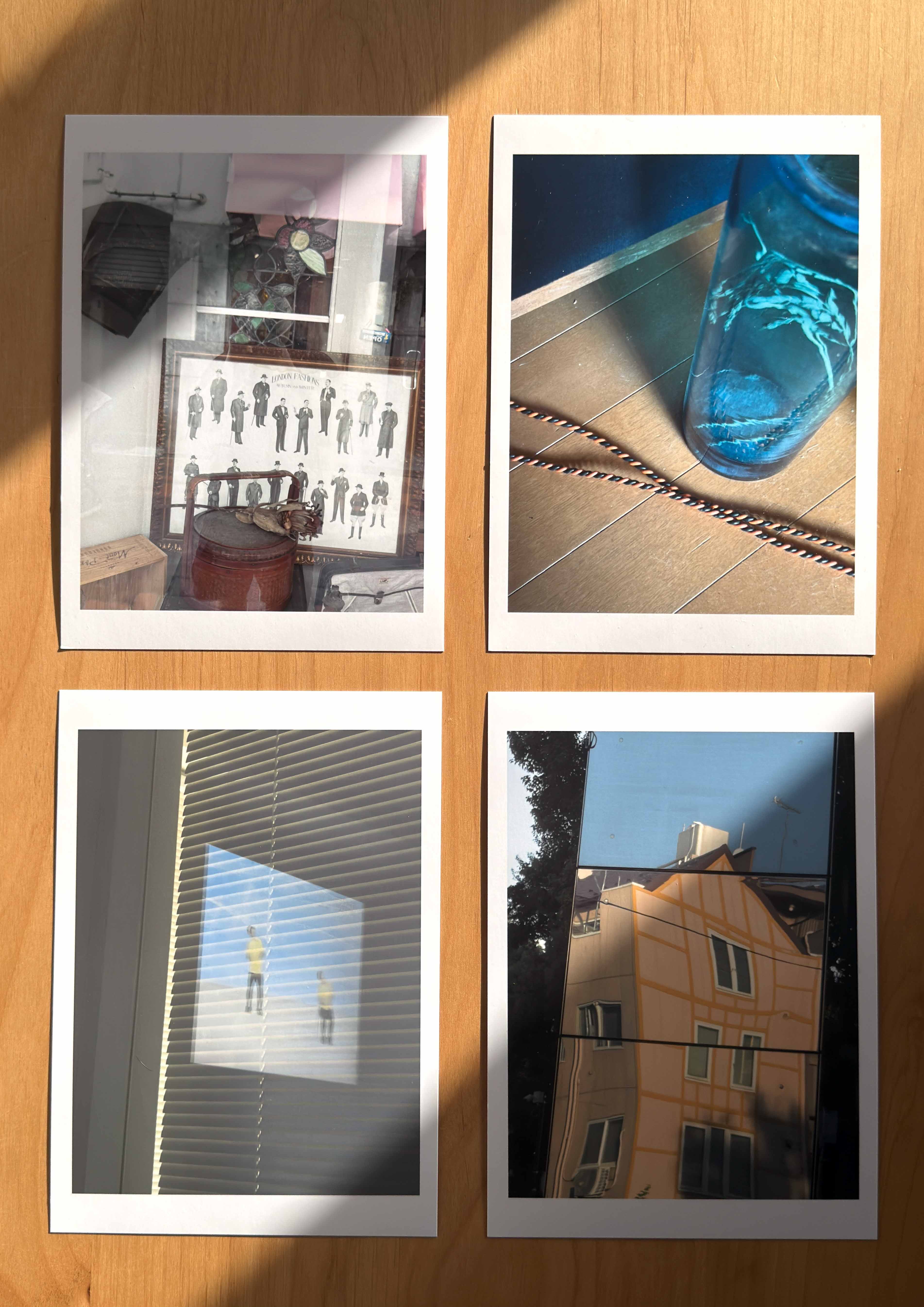 Four photographic prints laid out on a wooden surface, showing a vintage display with framed illustrations, a blue glass vase on wooden floor, a projection on window blinds, and a distorted reflection of a yellow house on a shiny surface.