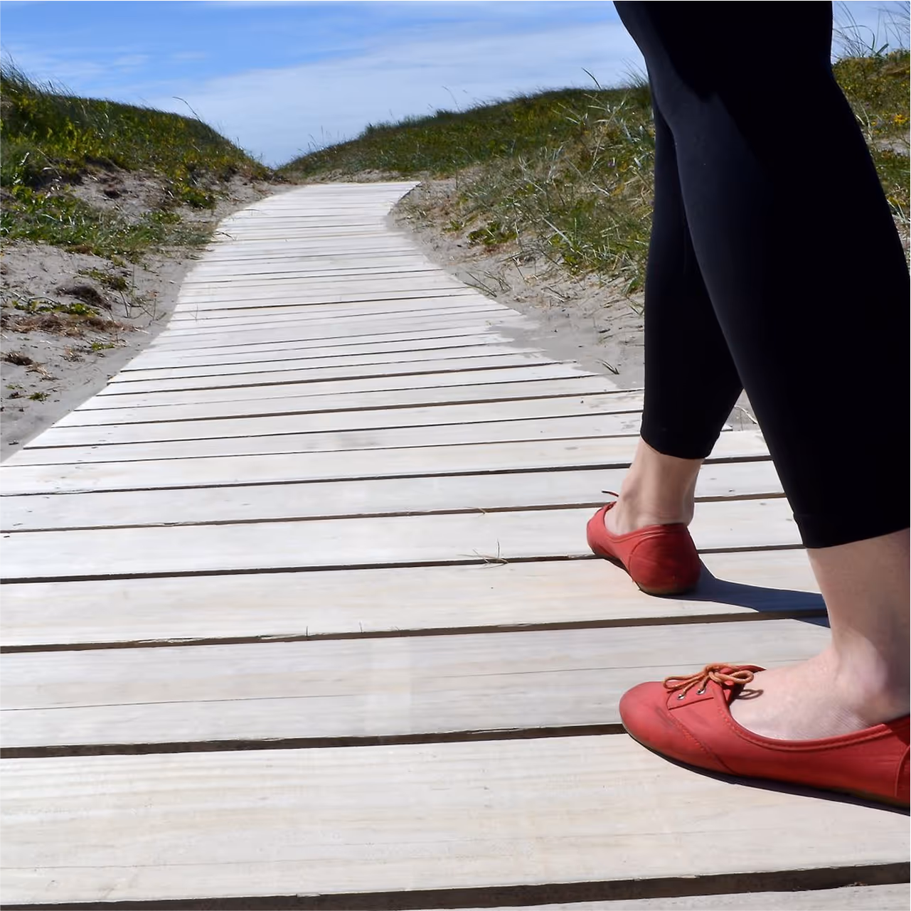 Women in red flat shoes walking on accoya decking near a beach