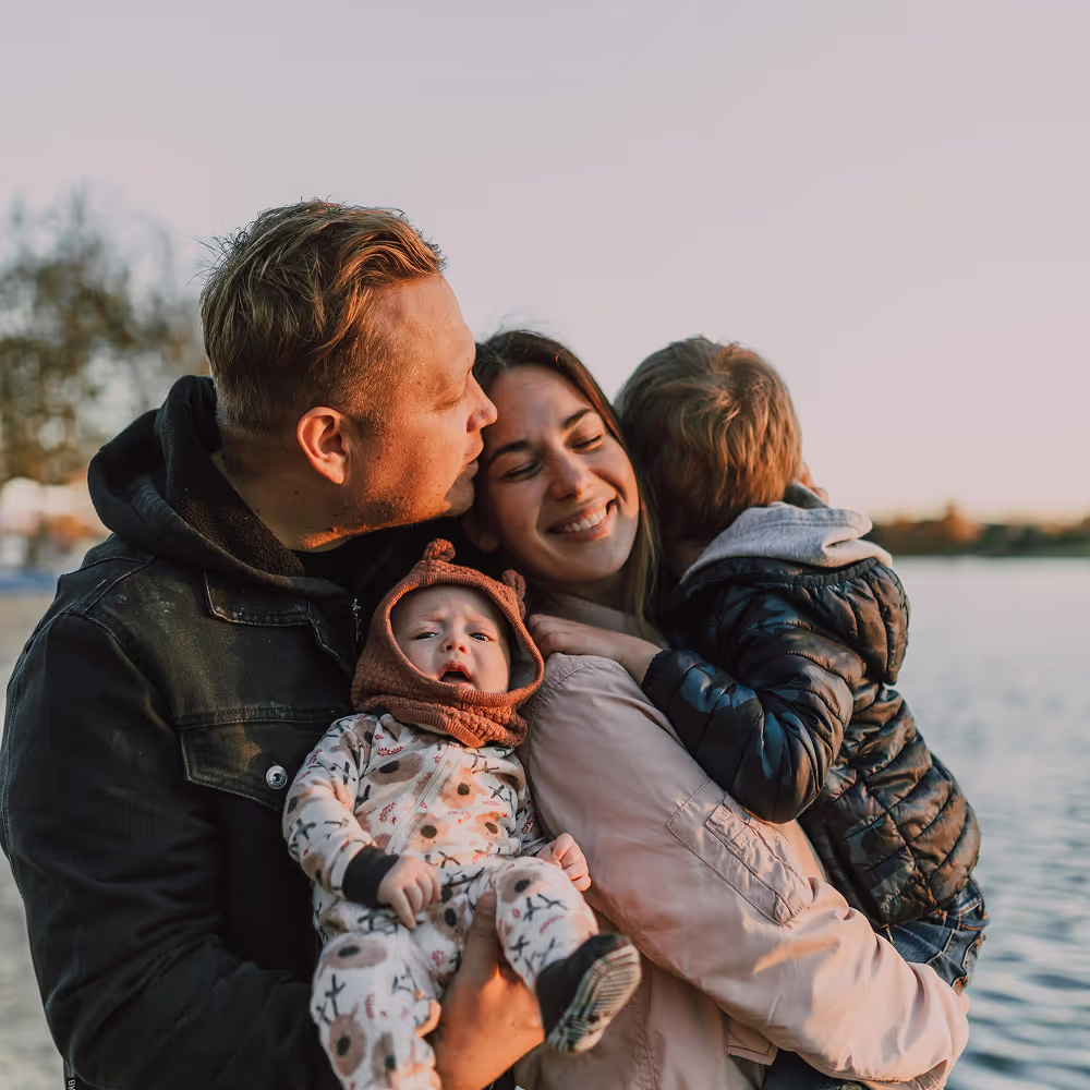 Young endearing couple with young kids all sharing a tight embrace